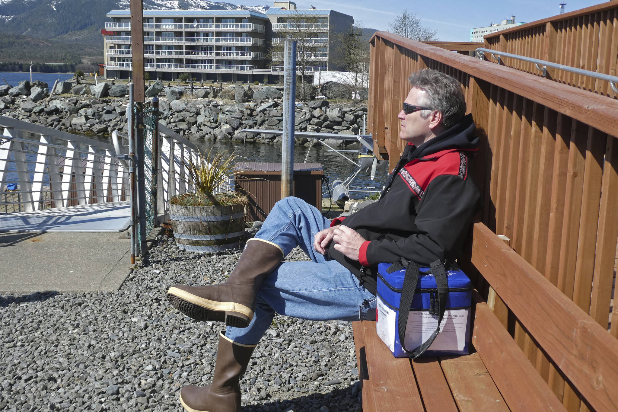 Gov. Mike Dunleavy sits beside a case containing COVID-19 vaccine doses as he waits near a floatplane dock on Thursday, April 22, 2021, in Ketchikan, Alaska. State health officials have said Alaska has an ample supply of COVID-19 vaccines, and Dunleavy, who flew from Ketchikan to Hyder, Alaska, said he wanted to offer vaccines not only to residents of Hyder but also to Canadians across the border from Hyder in Stewart, British Columbia. (AP Photo/Becky Bohrer)