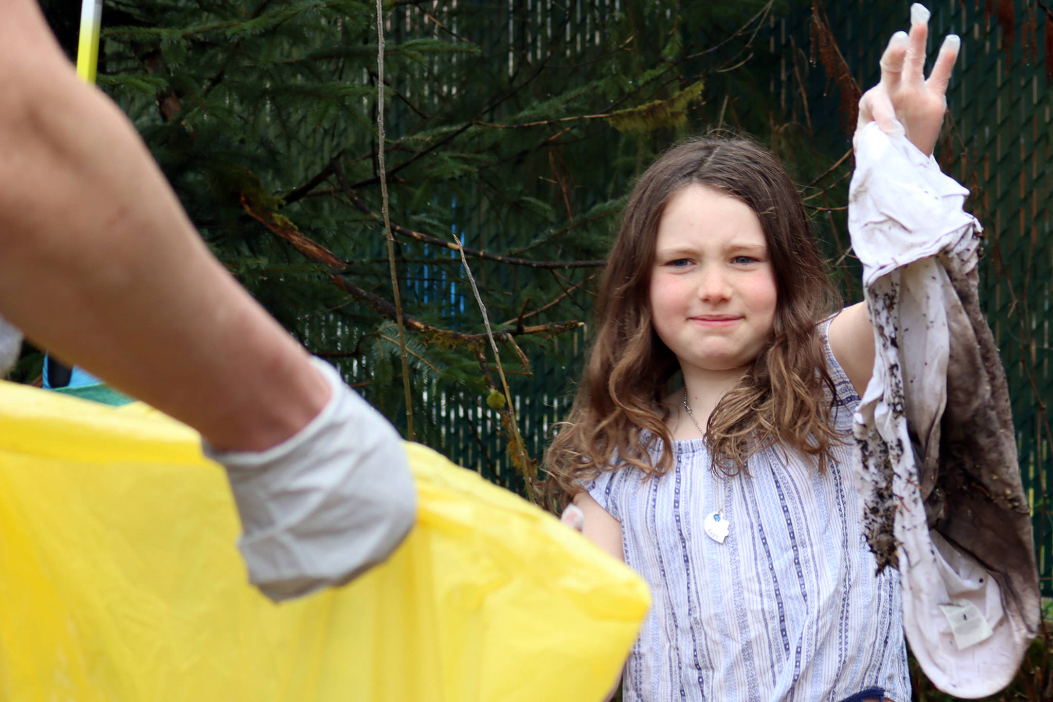 Nora Baldwin, 8, a member of Girl Scout Troop 4009, carries a dirty shirt found on the side of Mendenhall Loop Road in between gloved fingers toward a litter bag on Saturday, May 1, 2021. (Ben Hohenstatt / Juneau Empire)