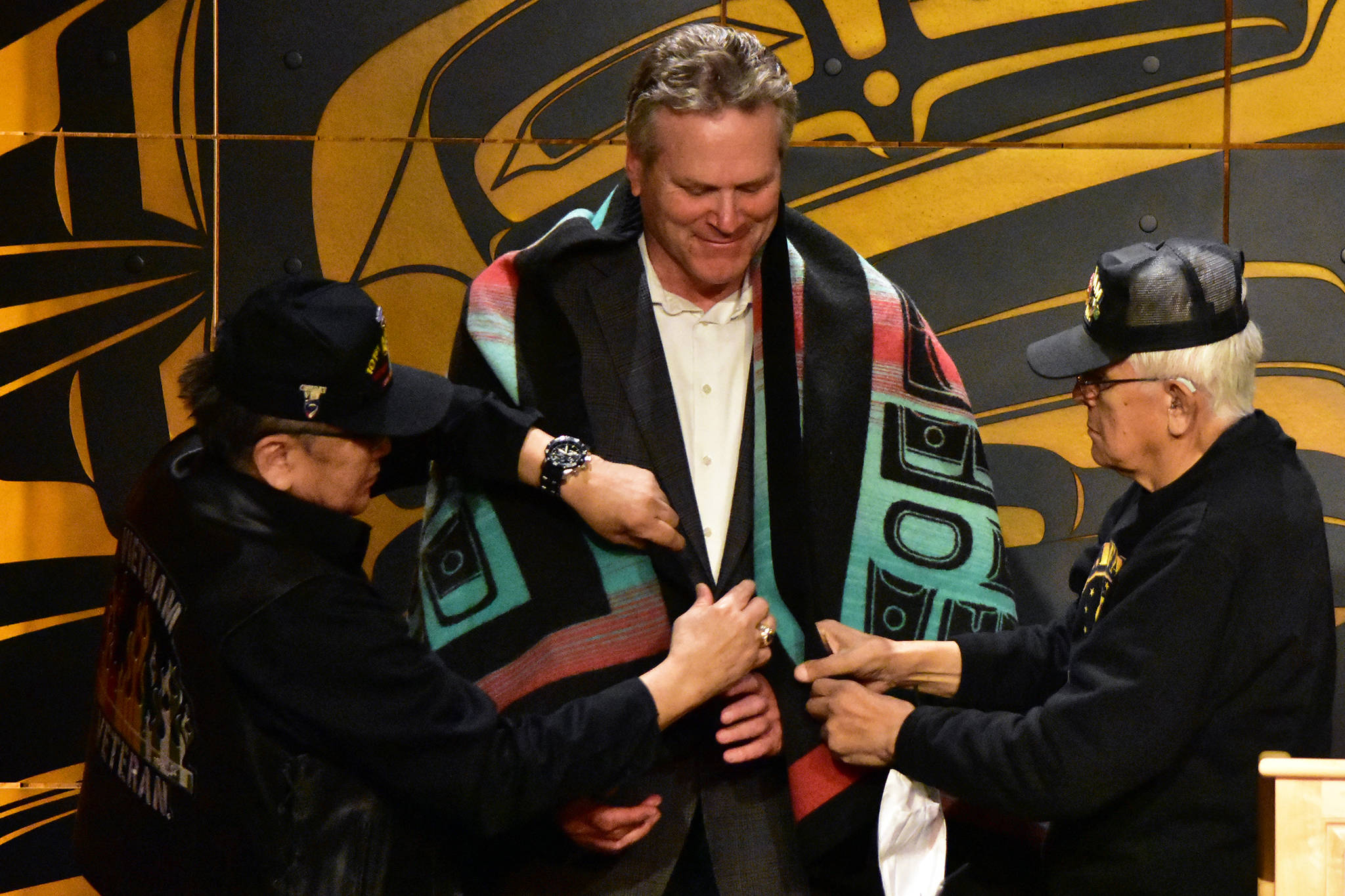 Alaska Native Vietnam War veterans James Lindoff, left and George Bennett, right, drape a ceremonial blanket over Gov. Mike Dunleavy, center, during a news conference on Wednesday, May 5, 2021. Dunleavy is proposing a program allowing Alaska Native veterans to exchange federal land for state lands potentially closer to their homes. (Peter Segall / Juneau Empire)