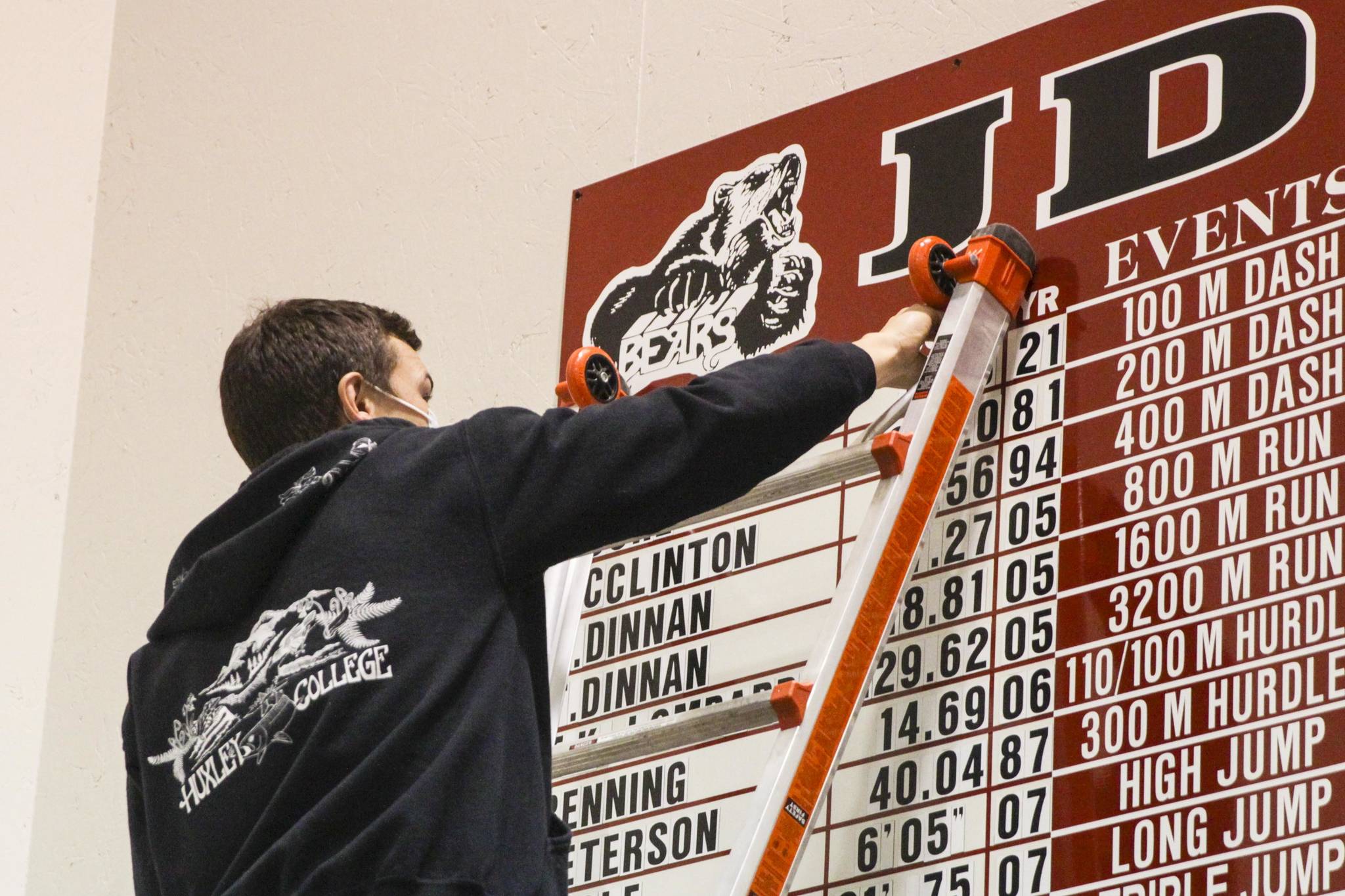 Zack Pursell, assistant coach for the Juneau-Douglas High School: Yadaa.at Kalé track team, puts James Connally’s name on the school record board for breaking a long-standing record for the 100 meter dash on May 11, 2021. (Michael S. Lockett / Juneau Empire)
