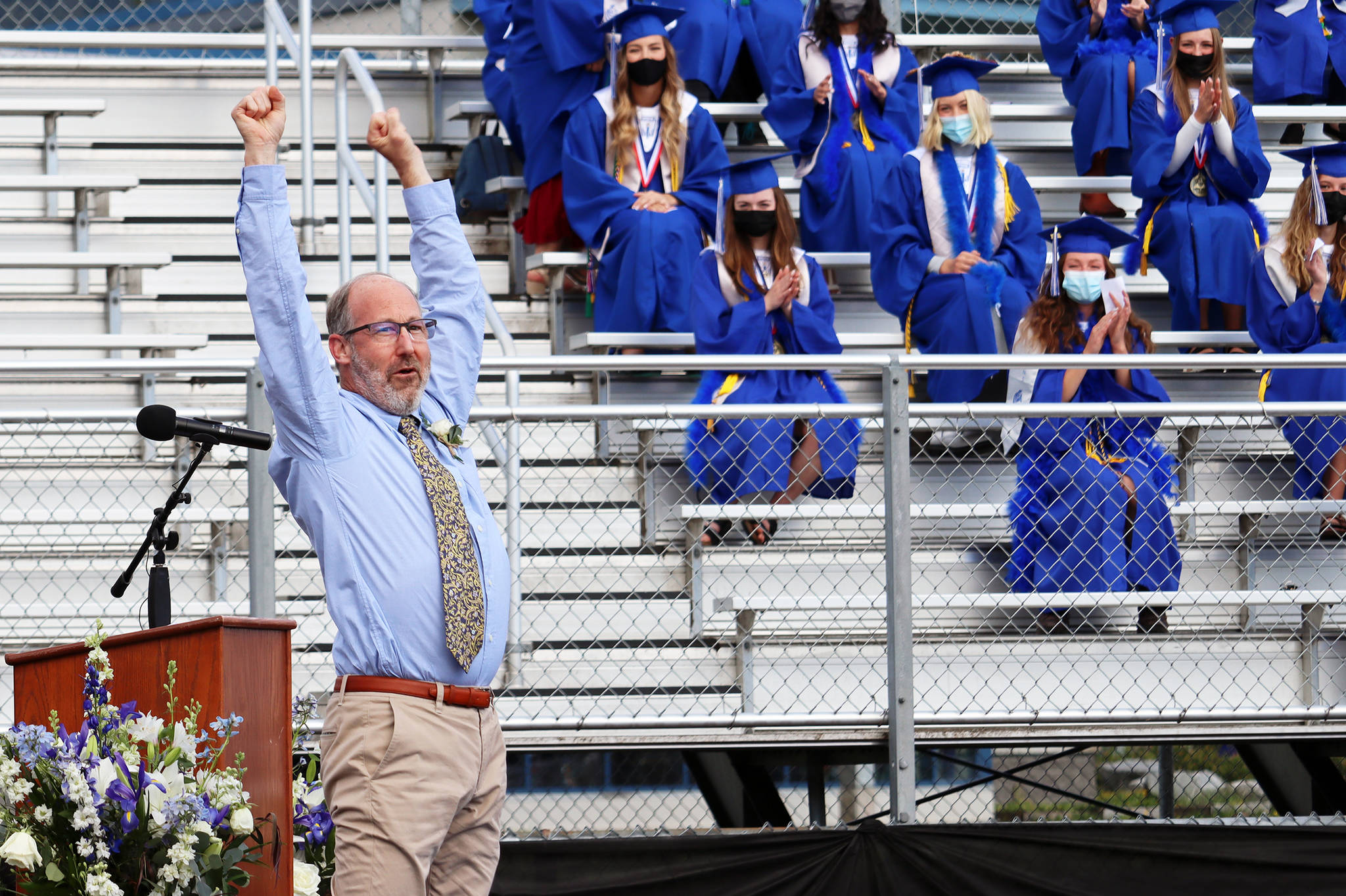 TMHS history teacher James Marks raises his arms in triumph after turning a cartwheel to begin his teacher address during the graduation ceremony held Sunday, May 23, 2021 at TMHS. Marks said while students may forget what he said, they’ll always remember the cartwheel. In his speech, Marks said the challenging school year had included gifts such as lives saved by distancing, science and technology, personal learning and strength. He advised students to always look for the helpers, as Fred Rogers said, not to let setbacks set them back and to work to create their own futures. (Ben Hohenstatt / Juneau Empire)