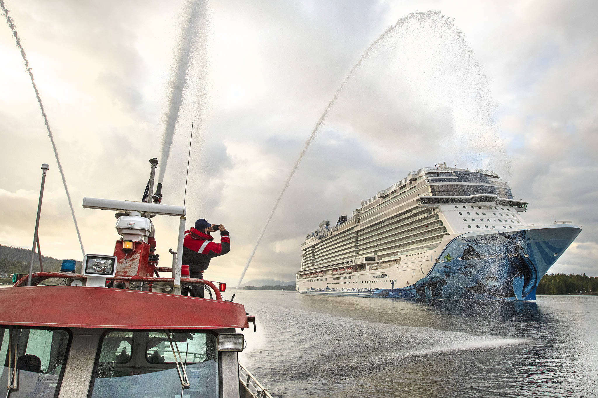 Firefighter medic Andy Tighe snaps a photo of the breakaway plus-class cruise ship Norwegian Bliss while Captain Tracy Mettler operates a fireboat in the Tongass Narrows in Ketchikan, Alaska, on June 4, 2018. President Joe Biden signed into law Monday, May 24, 2021, legislation that opens a door for resumed cruise ship travel to Alaska after the pandemic last year scrapped sailings. (Dustin Safranek/Ketchikan Daily News)