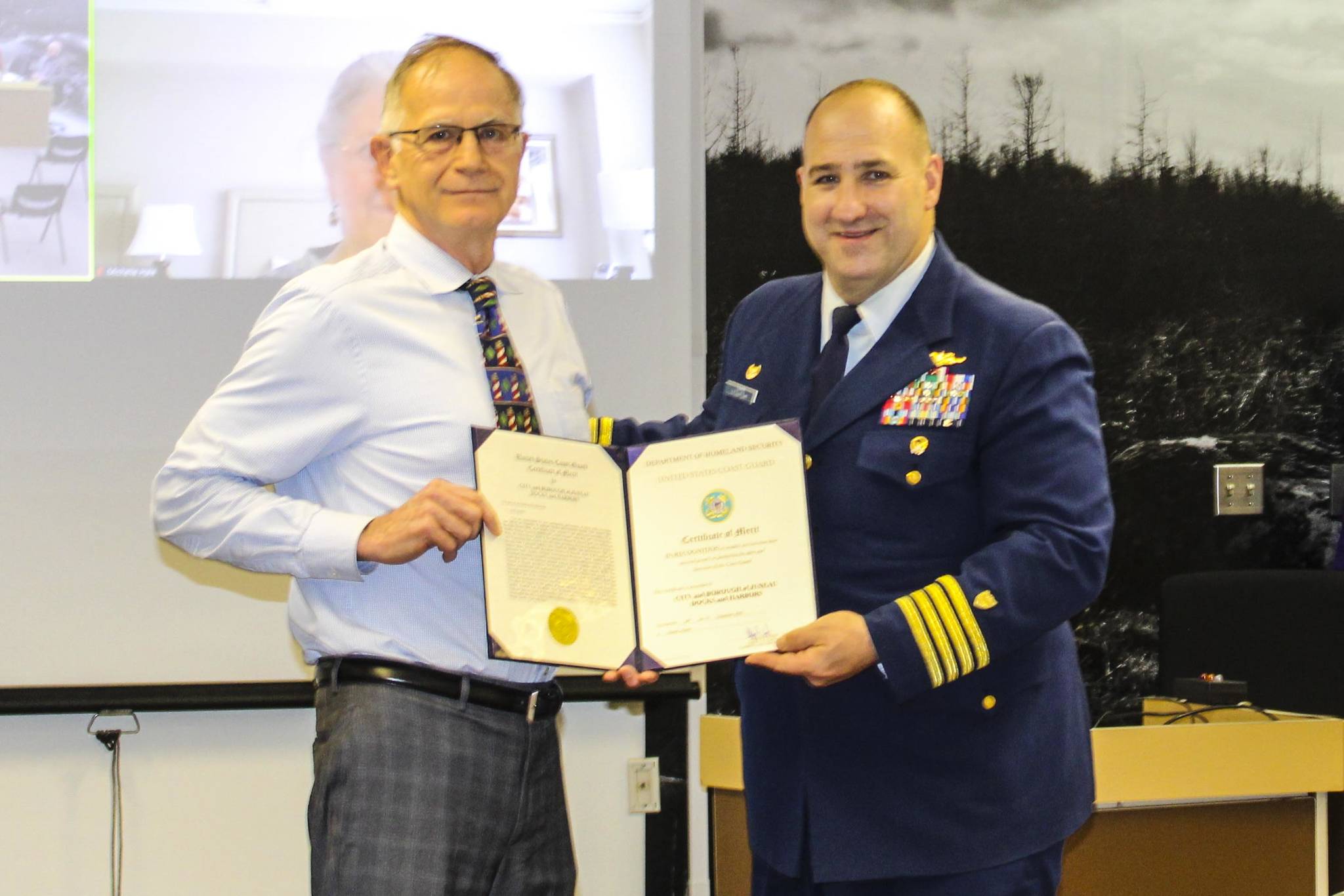 Capt. Stephen White, right, presents a commendation to City and Borough of Juneau Docks and Harbors port director Carl Uchytil during an Assembly meeting on May 24, 2021. (Dana Zigmund / Juneau Empire)