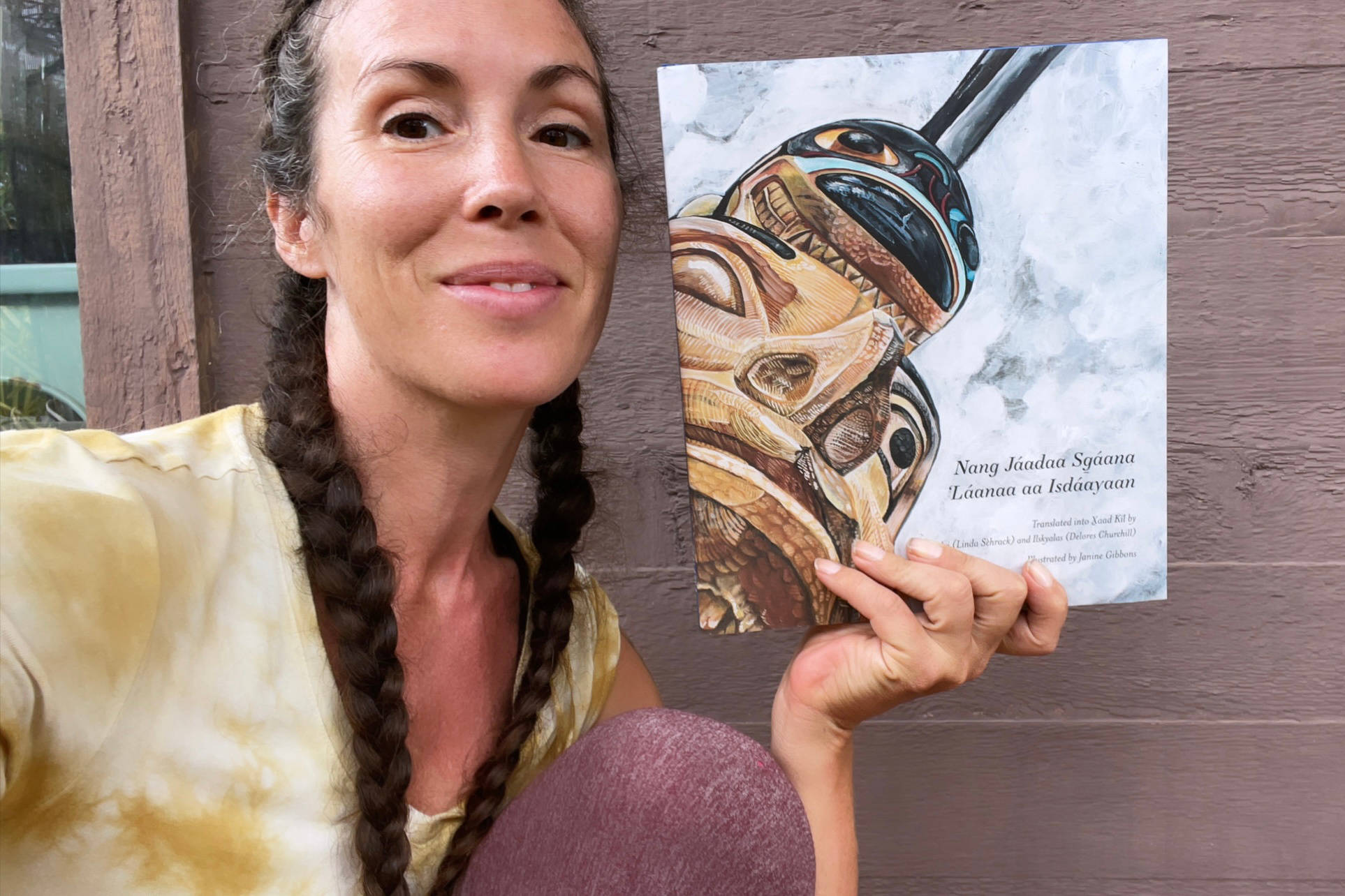 Haida artist Janine Gibbons poses with the book she illustrated, the Sealaska Heritage Institute’s first children’s book in the Haida language Xaad Kíl, a translation of the traditional story “The Woman Carried Away by Killer Whales.” (Courtesy photo / Janine Gibbons)