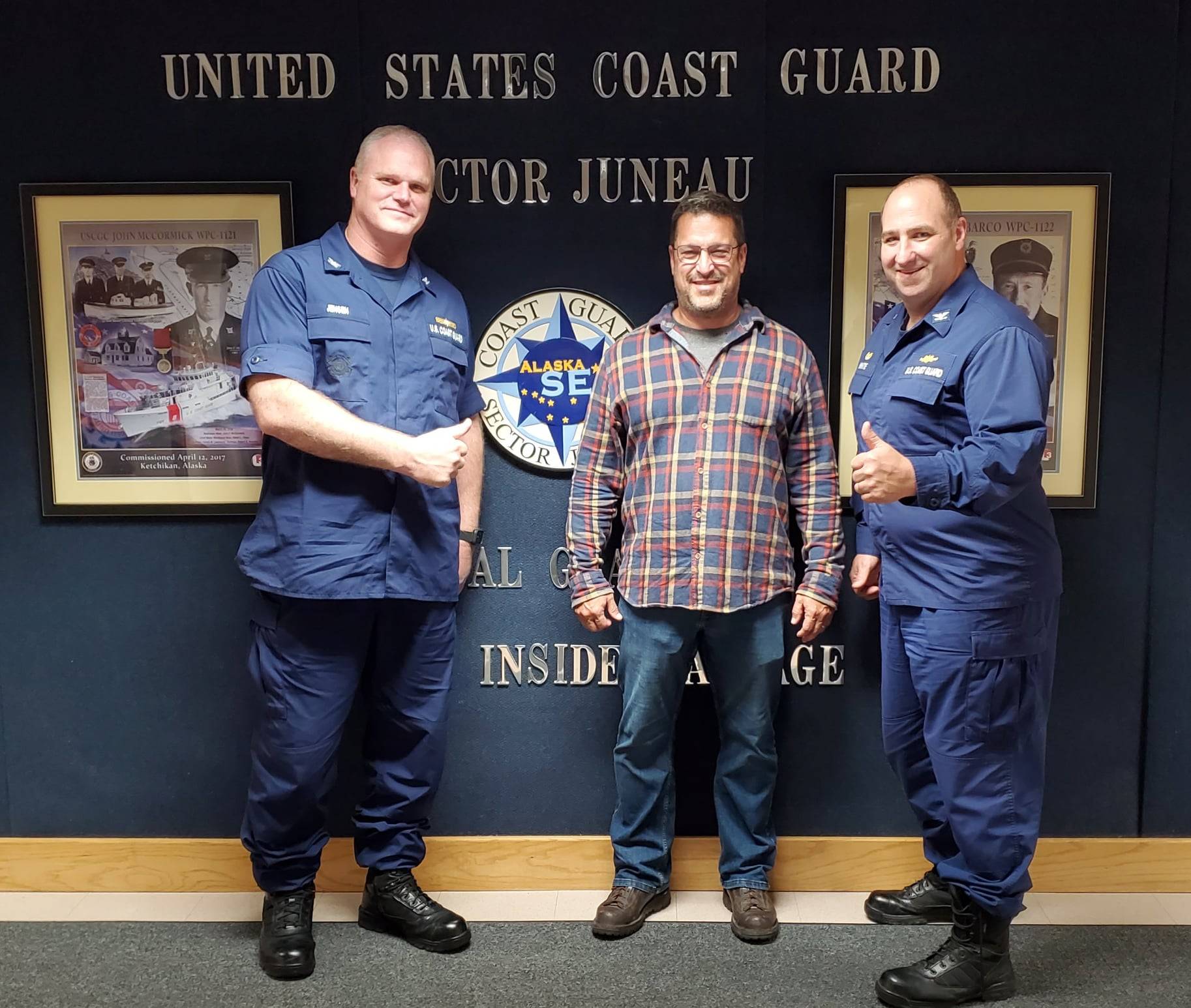 Incoming Coast Guard Sector Juneau commander Capt. Darwin A. Jensen, left, and outgoing commander Capt. Stephen R. White, right, congratulate Herman Cestero, center, for his quick action in rescuing a fisherman in distress on June 24, 2021. (Michael S. Lockett / Juneau Empire)