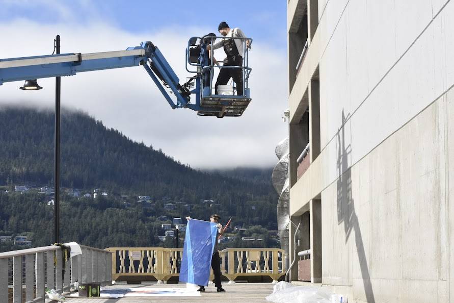 Artists work to hang a 60-by 25-foot mural depicting Elizabeth Kaaxgal.aat Peratrovich on the south wall of the Marine Parking garage on Aug. 30. (Peter Segall/Juneau Empire)