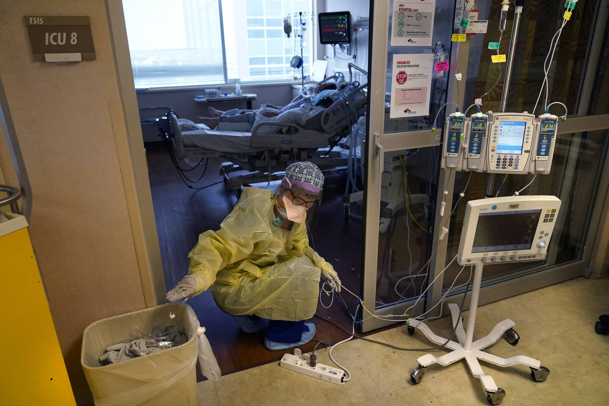An ICU nurse, moves electrical cords for medical machines, outside the room of a patient suffering from COVID-19, in an intensive care unit at the Willis-Knighton Medical Center in Shreveport, La. The COVID-19 pandemic has created a nurse staffing crisis that is forcing many U.S. hospitals to pay top dollar to get the help they need to handle the crush of patients this summer. (AP Photo/ Gerald Herbert)