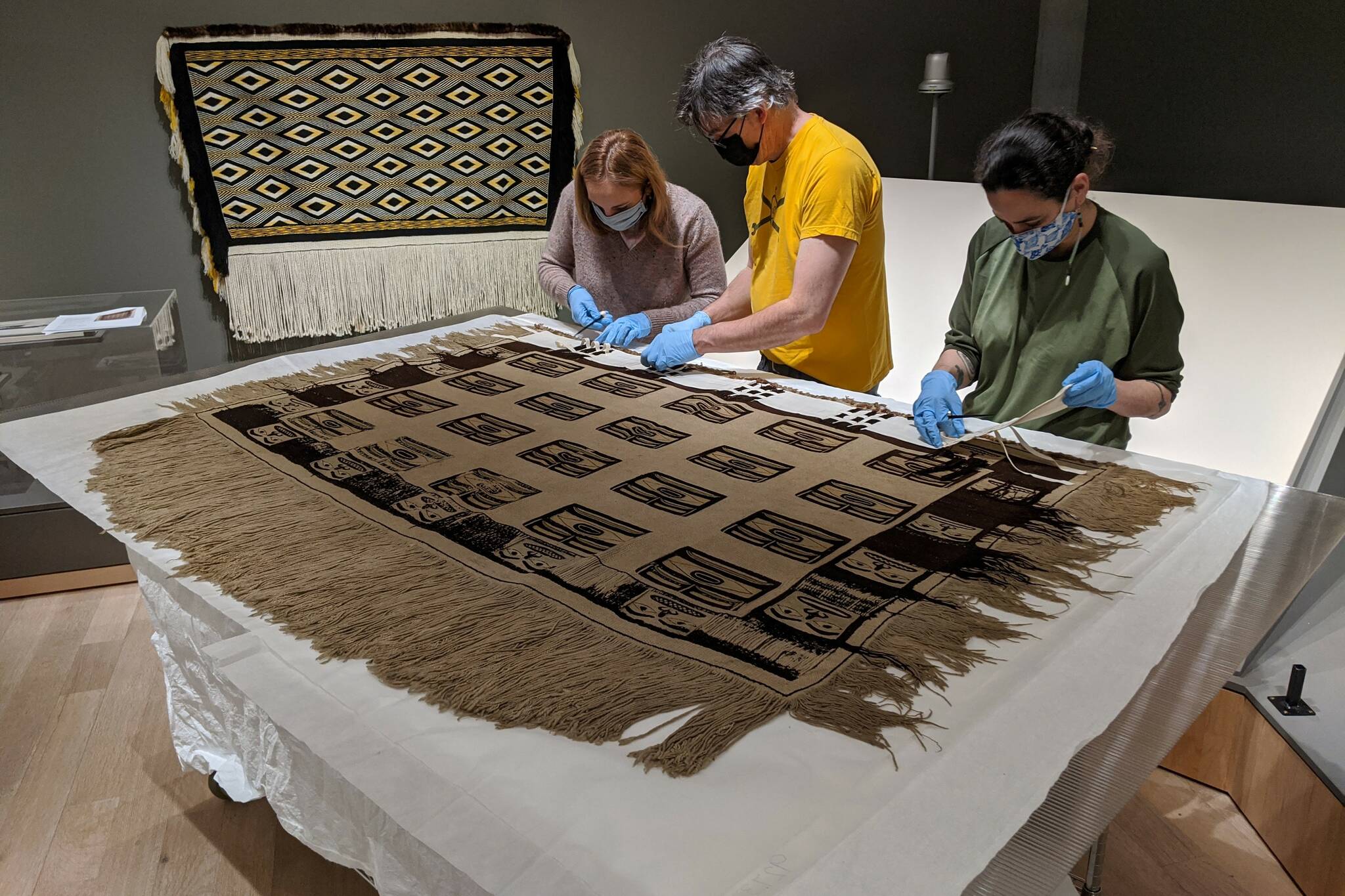 Courtesy Photo / Chelsea Kilgore, Alaska State Library Archives and Museum 
From left to right: Jackie Manning, curator of exhibits for the Alaska State Library, Archives and Museum; Aaron Elmore, exhibit designer, and Ellen Carrlee, conservator for the museum unpack an ancient raven’s tail robe on loan from the Royal Ontario Museum in Canada. This robe is one of only about a dozen older robes in existence, according to SLAM collections curator Steven Kenrikson, and will only be on display at SLAM until next month.