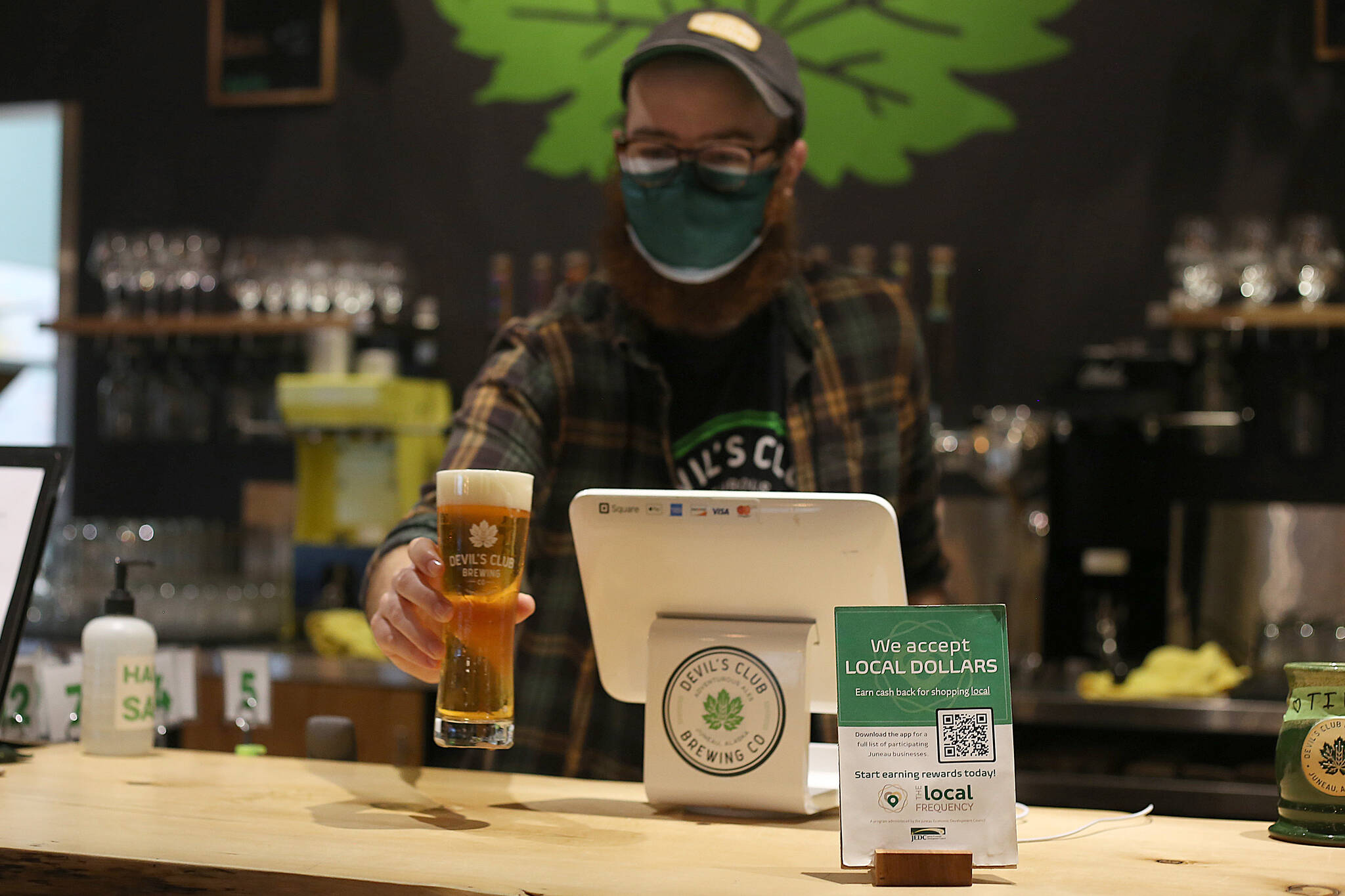 A Devil's Club Brewing Co. employee serves up a beer behind a sign promoting Local Frequency. The customer loyalty app is in the running for a 2021 Strong Communities Award. (Courtesy Photo)