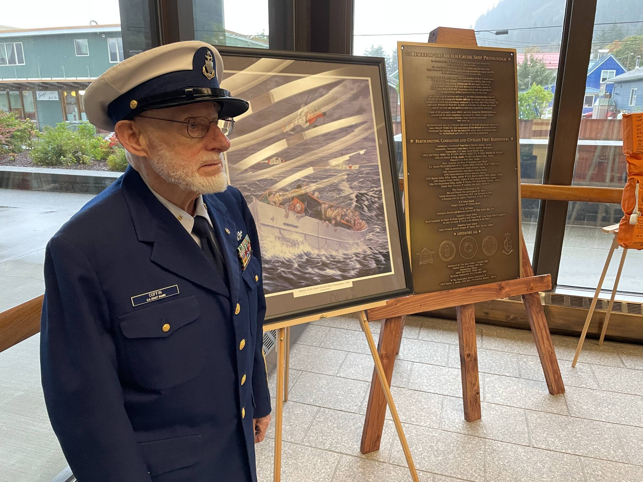 Senior Chief Petty Officer Eugene Coffin III, who helped coordinate the response to the Prinsendam fire from the Coast Guard District 17 watch center, stands next to the plaque commemorating the rescue in the lobby of the Hurff A. Saunders Federal Building on Sept. 23, 2021. (Michael S. Lockett / Juneau Empire)