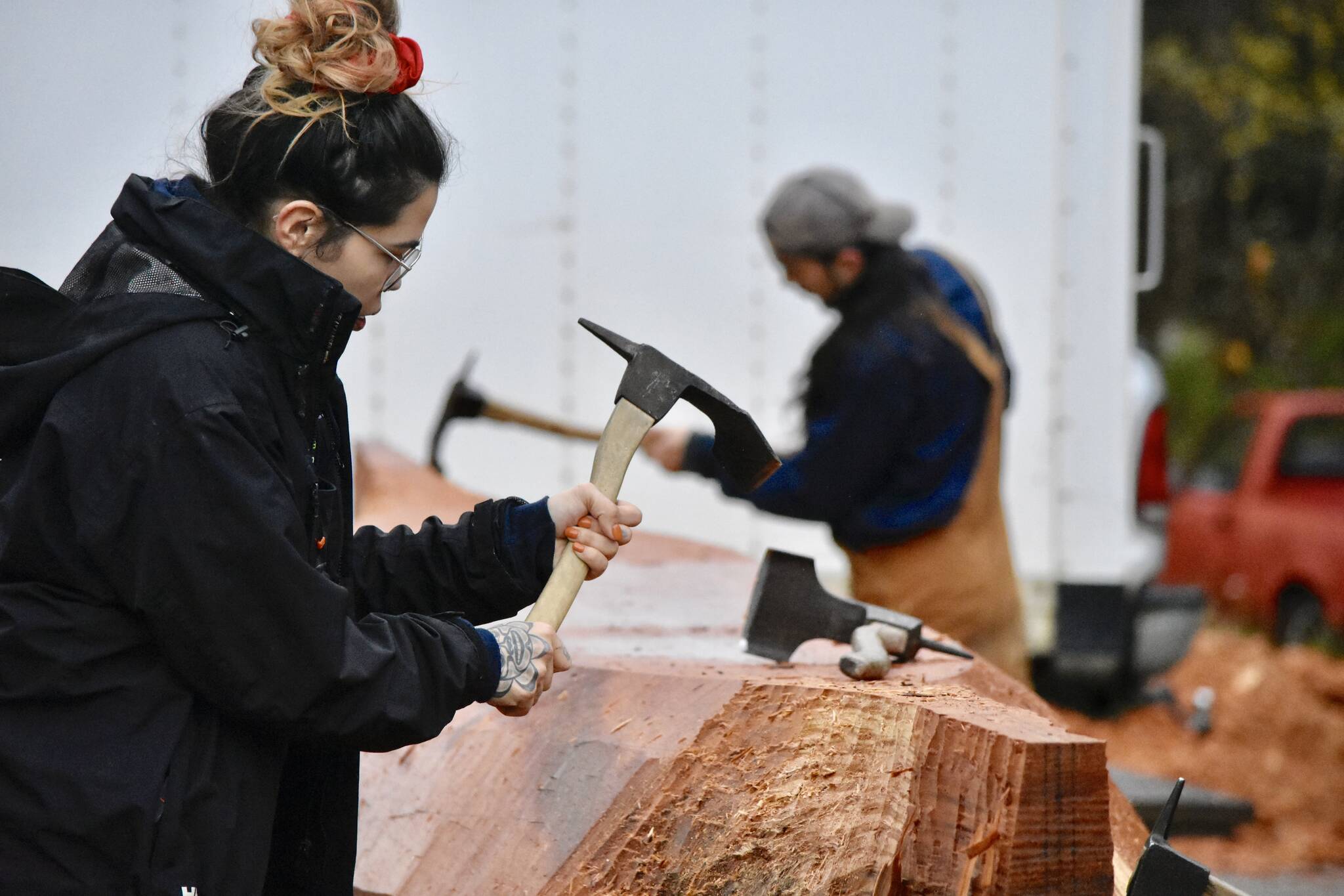 University of Alaska Student Skaydu.û Jules, carves a red cedar log under the supervision of Tlingit master carver Wayne Price in the parking lot of Angoon High School on Tuesday, Oct. 26, 2021. Jules a member of the Teslin Tlingit Council, a self-governing First Nation based in Teslin in Southern Yukon Territory, Canada, and said she wants to become a Tlingit language teacher. (Peter Segall / Juneau Empire)
