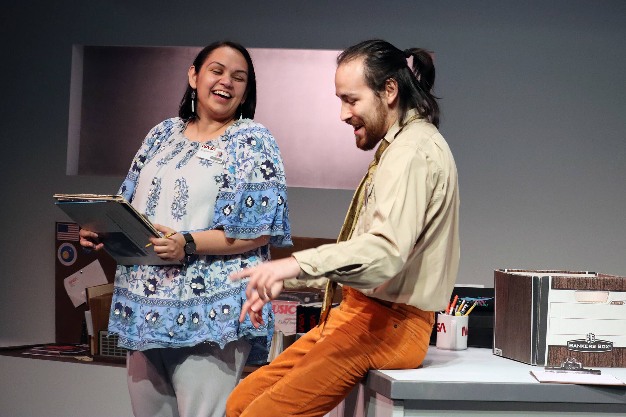 Sarah (Erin Tripp) and Carl (Jared Olin) laugh while working on the Voyager project during a dress rehearsal for Perseverance Theatre’s “Voyager One.” The play, which is running now, is simultaneously two period pieces. One is set in the ’70s, the other is in the distant future. (Ben Hohenstatt / Juneau Empire)