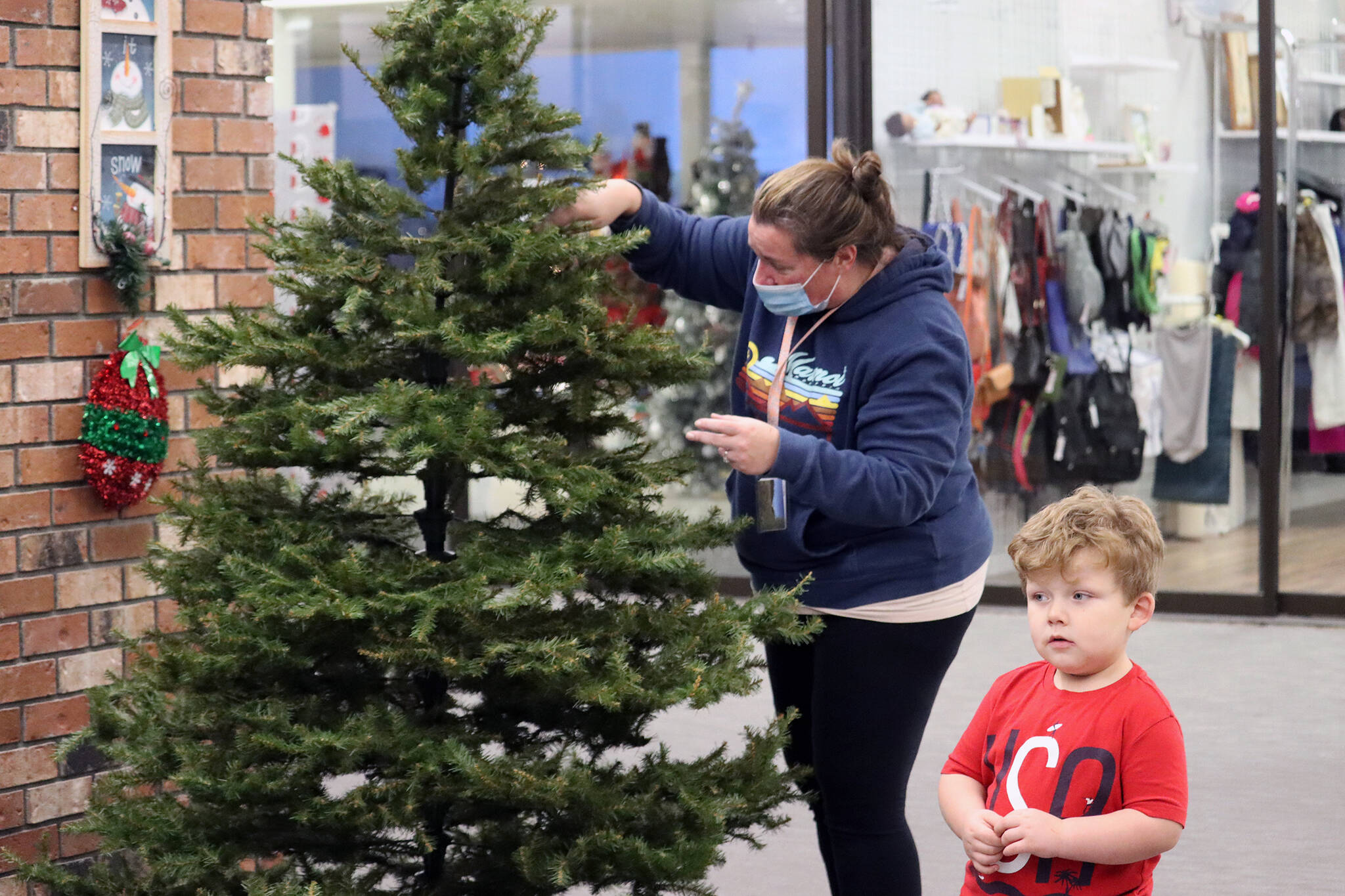 Sandra Mulkey and her son Caleb, 3, set up a Christmas tree at the Mendenhall Mall on Nov. 24. Mulkey is kicking off a toy drive for foster children. She said that she has not collected toys at the Mendenhall Mall for the last few years because of low traffic. However, she said the increased traffic at the now mostly-full mall prompted her to set up there. (Dana Zigmund/Juneau Empire)