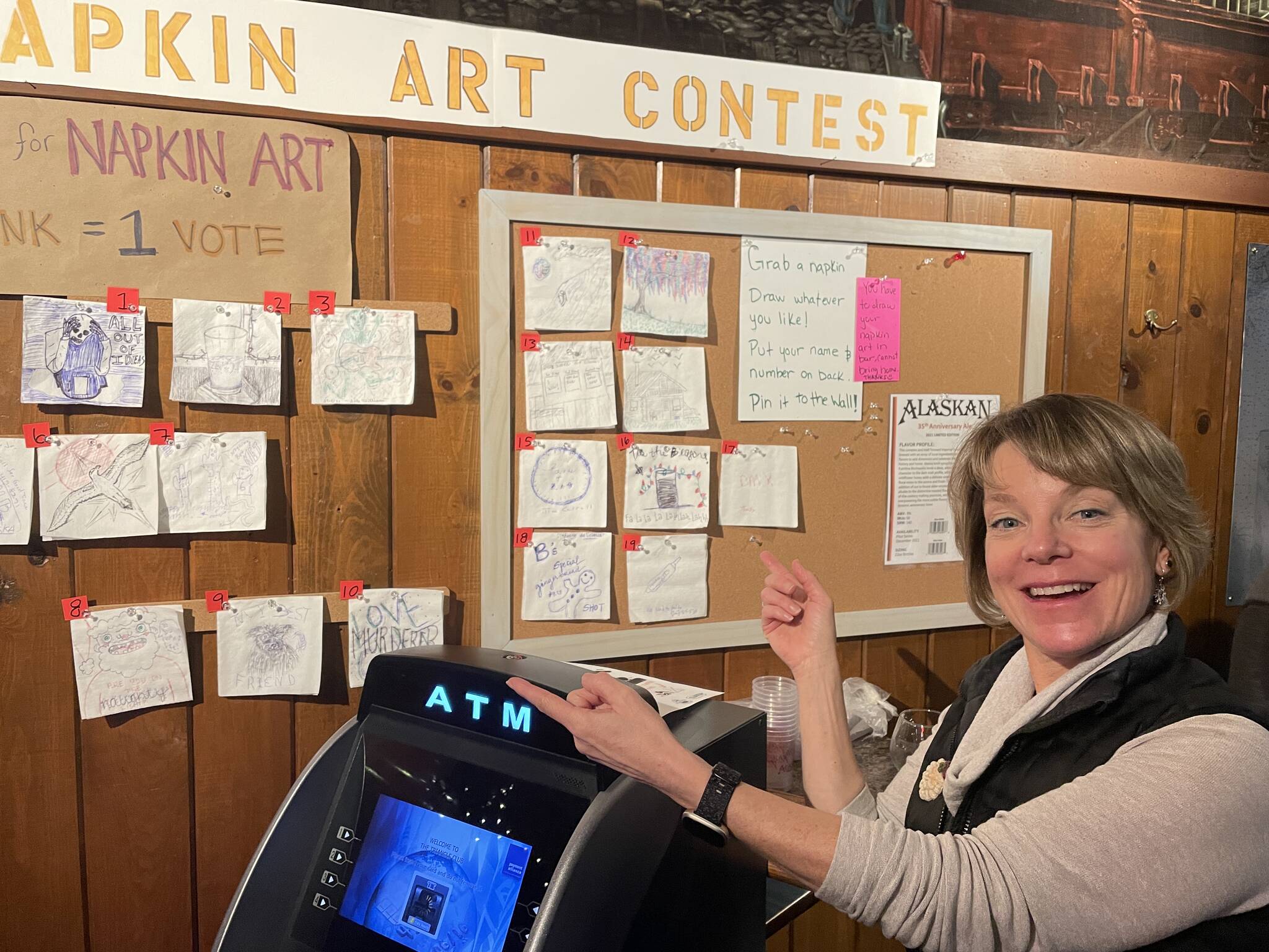 Triangle Club Bar owner Leeann Thomas shows off some of the art for the bar’s Napkin Art Contest during Gallery Walk on Dec. 3, 2021. (Michael S. Lockett / Juneau Empire)