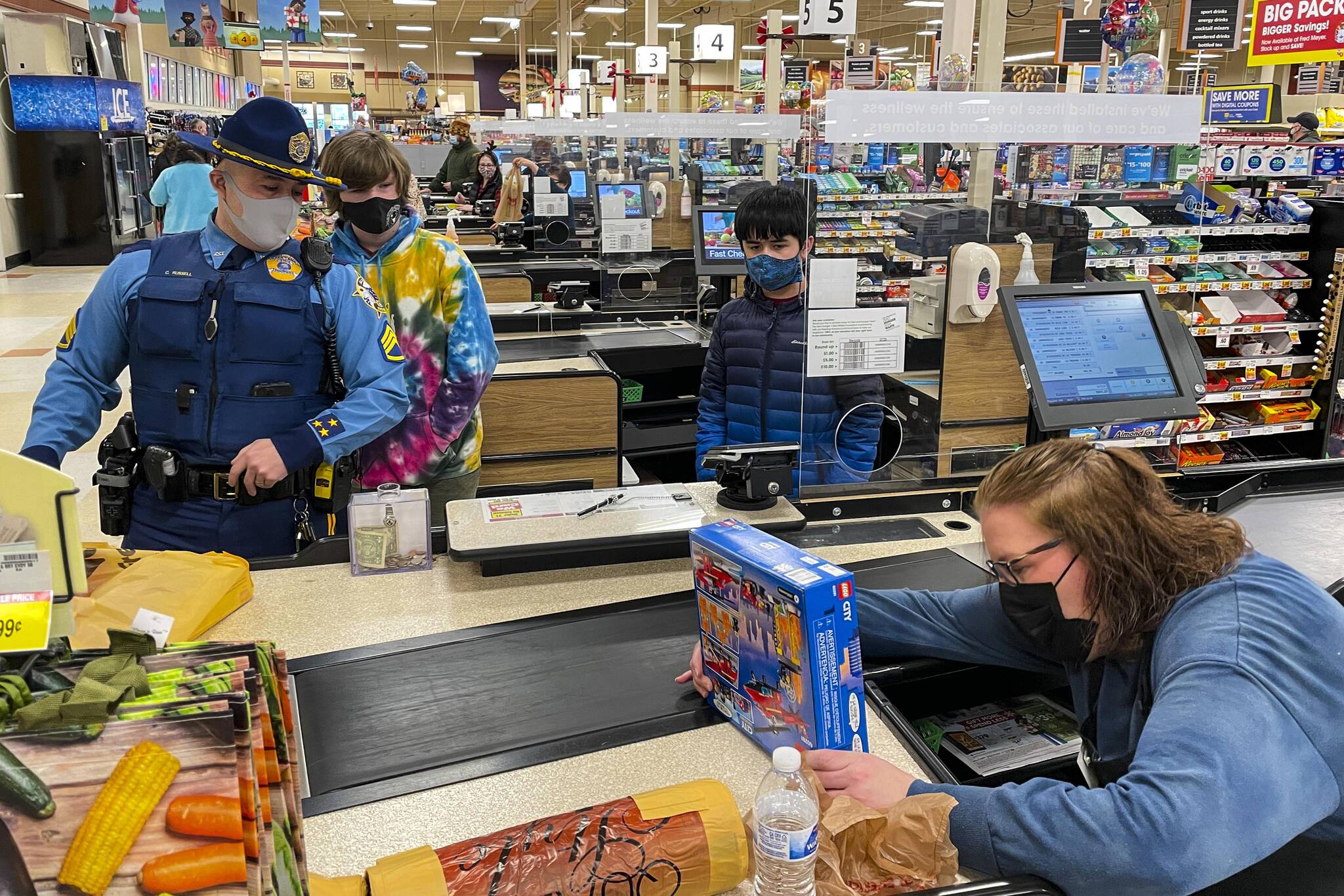 Alaska State Trooper Patrol Sergeant Chris Russell, Weldon and Keane look on as Fred Meyer employee Judy Magalotti checks them out during the annual Shop with a Cop event on Dec. 18, 2021. (Michael S. Lockett / Juneau Empire)