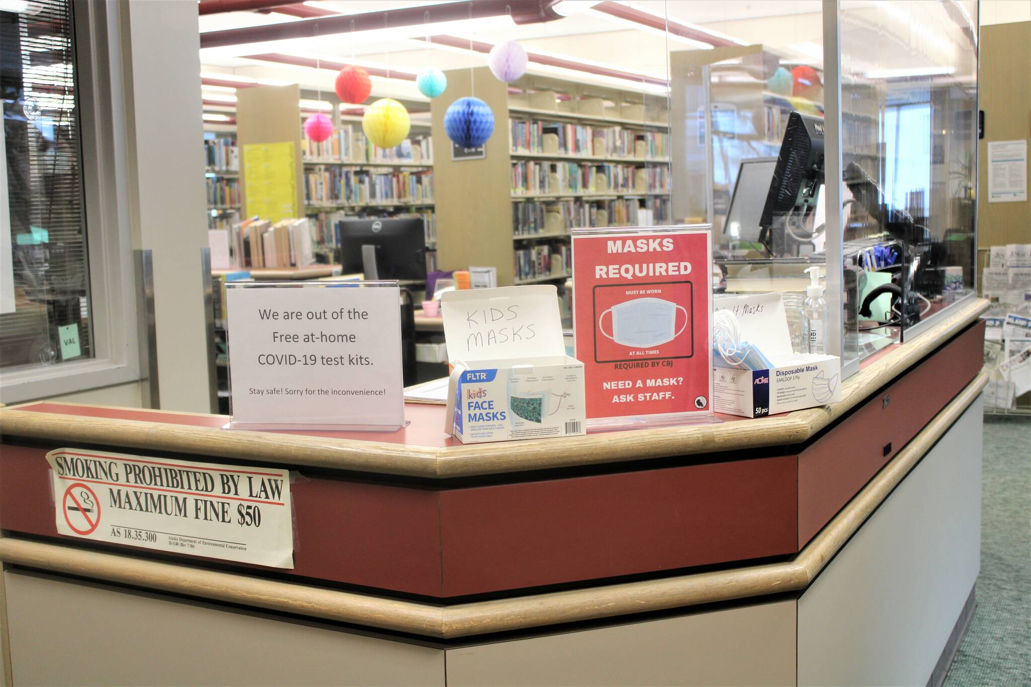 A collection of signs advising patrons about various COVID-related issues sits atop the front desk at the Douglas Branch of the Juneau Public Library on Jan. 6. (Dana Zigmund/Juneau Empire)