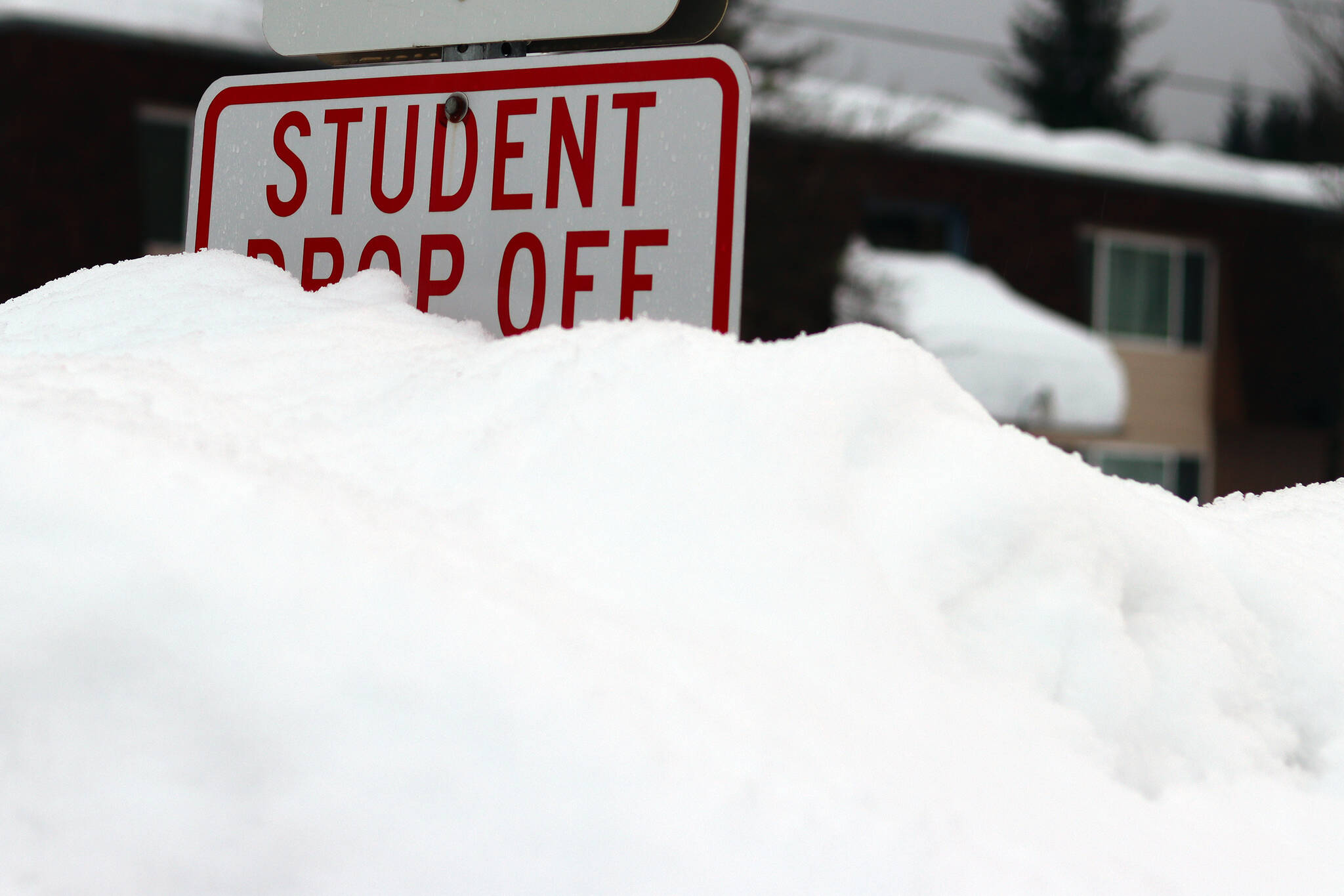 A mound of a snow obscures a “student drop off” sign near Sít’ Eetí Shaanàx-Glacier Valley School. School officials announced on Monday that classes were canceled for Tuesday due to weather. (Ben Hohenstatt / Juneau Empire)