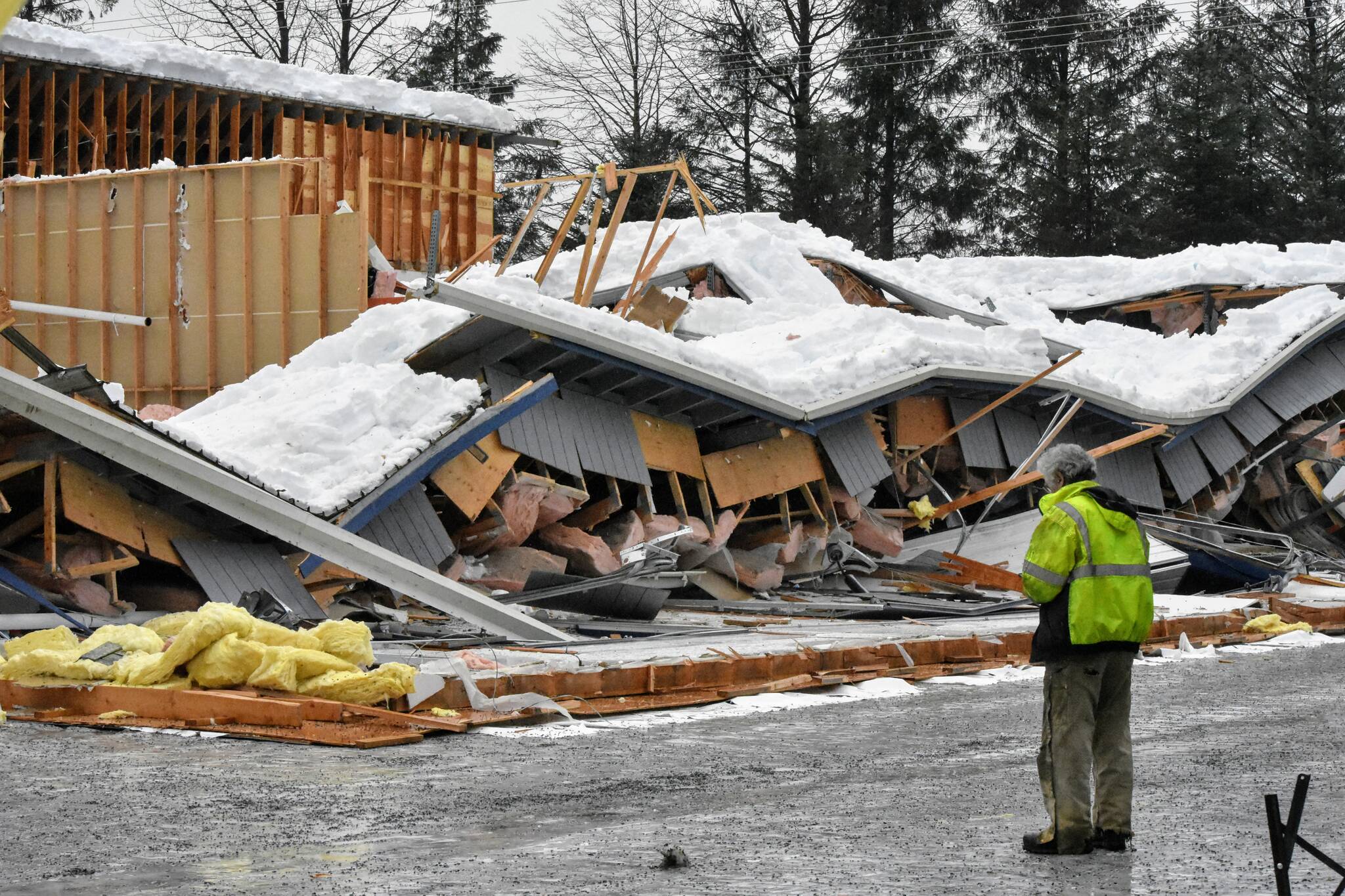 A worker stands outside a collapsed building in Lemon Creek on Tuesday, Jan. 11, 2022, one of two building collapses reported in Juneau amid ongoing rain following heavy snowfall. The City and Borough of Juneau said no injuries were reported and urged building owners to be cautious of snow loads on roofs. (Peter Segall / Juneau Empire)