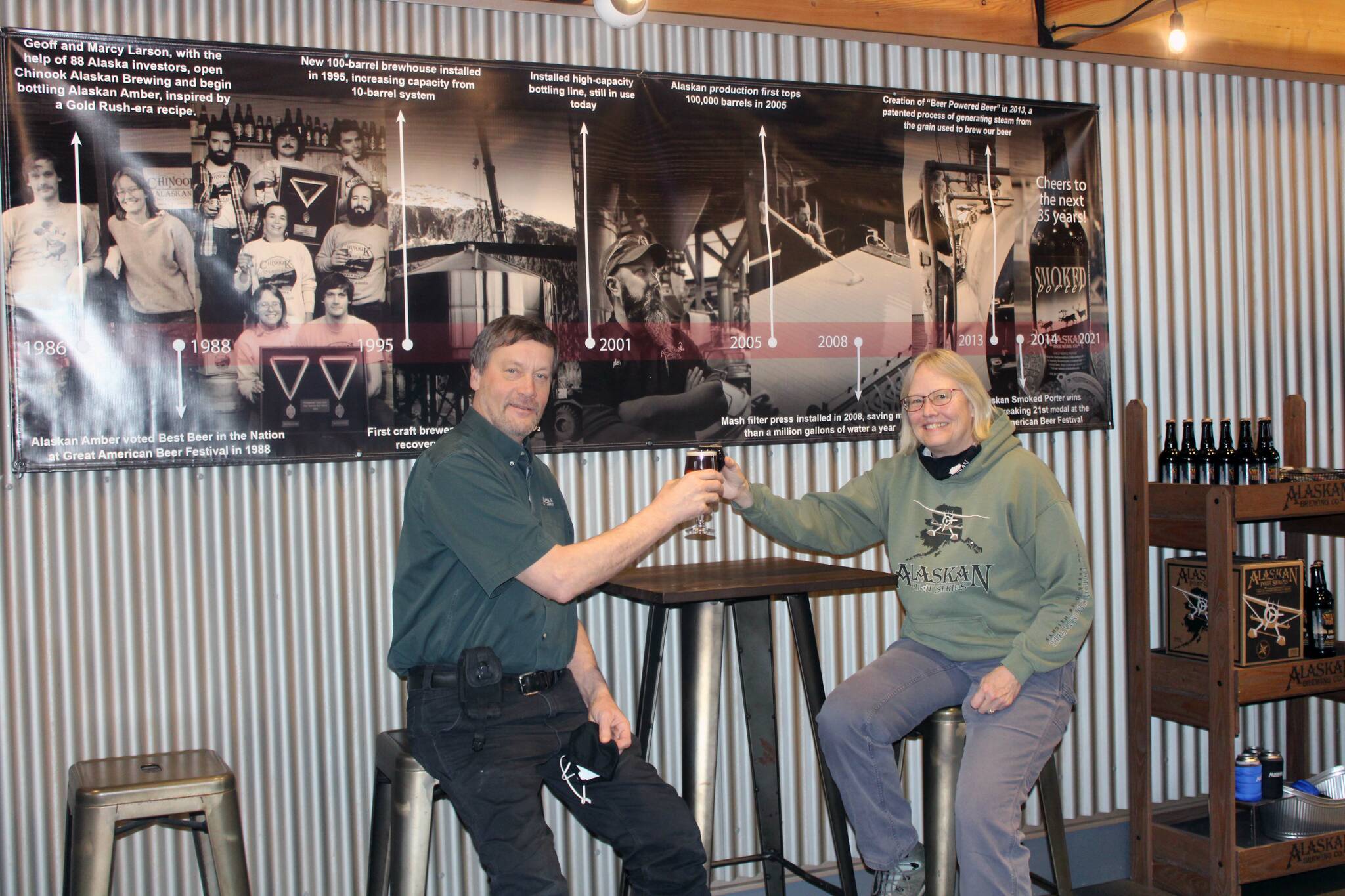 Dana Zigmund / Juneau Empire
Geoff and Marcy Larson toast to 35 years of brewing in the Alaskan Brewing Co. Tap Room on Feb. 4. A timeline of business milestones hangs behind them.