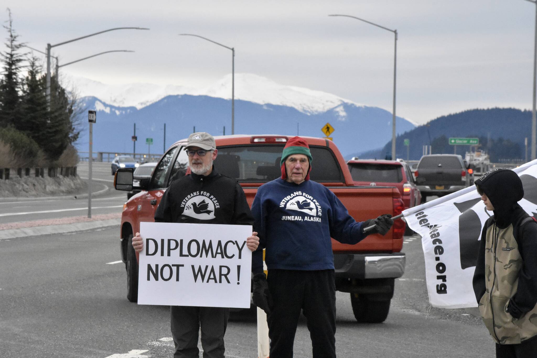 Juneau members of Veterans for Peace Craig Wilson, left, and K.J. Metcalf, wave signs urging a diplomatic solution in Ukraine the morning of Tuesday, Feb. 22, 2022. (Peter Segall / Juneau Empire)