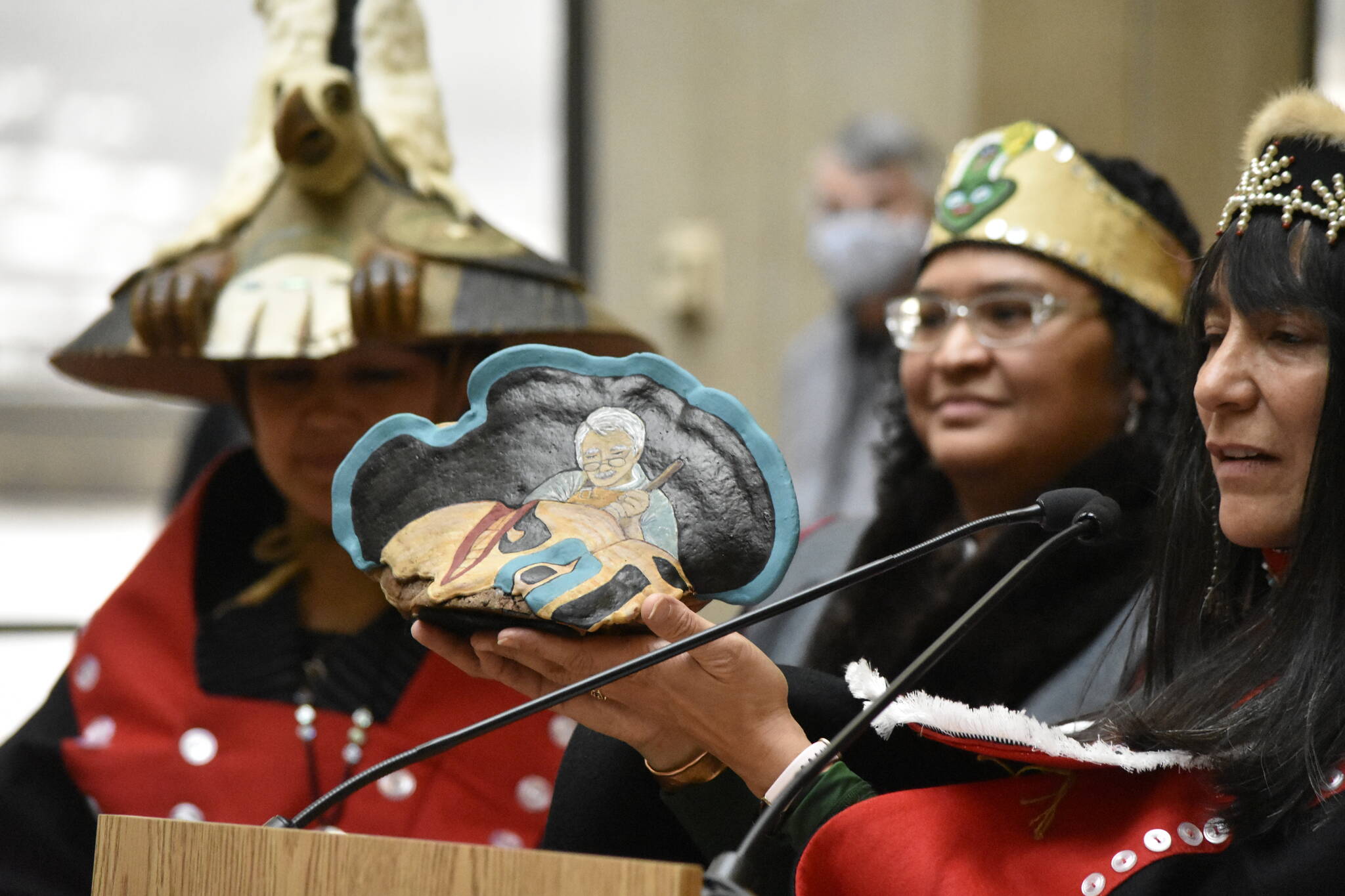 Kaasei Naomi Michalsen holds up a piece of painted cedar presented as a gift to Yéil Yádi Nathan Jackson at a celebration at the State Office Building on Friday, March 11, 2022, commemorating the re-installation of a totem pole carved by Jackson. (Peter Segall / Juneau Empire)