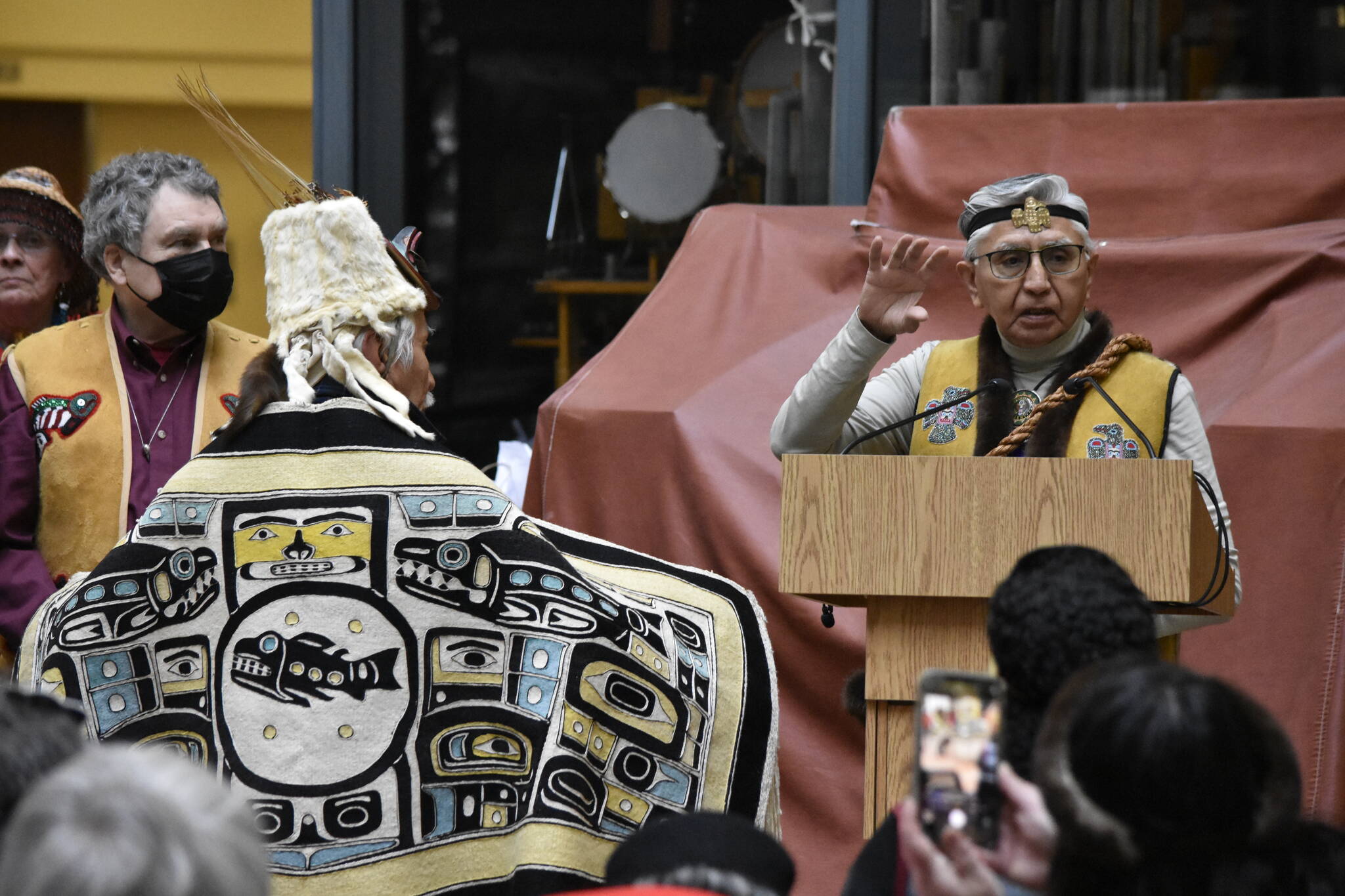 ḴiḴnkawduneek Paul Marks, Sr., right, speaks about the significance of the figures shown on a robe worn by Yéil Yádi Nathan Jackson, during a ceremony at the State Office Building on Friday, March 11, 2022. (Peter Segall / Juneau Empire)