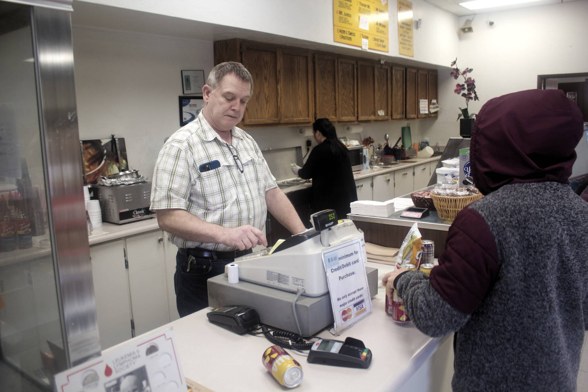 Neil Doogan, owner of J&J Deli and Asian Mart, rings up purchases while his wife Alma makes a sandwich for a customer Saturday. The deli that opened in 1979 is scheduled to close in August if a new owner can’t be found. (Mark Sabbatini / Juneau Empire)