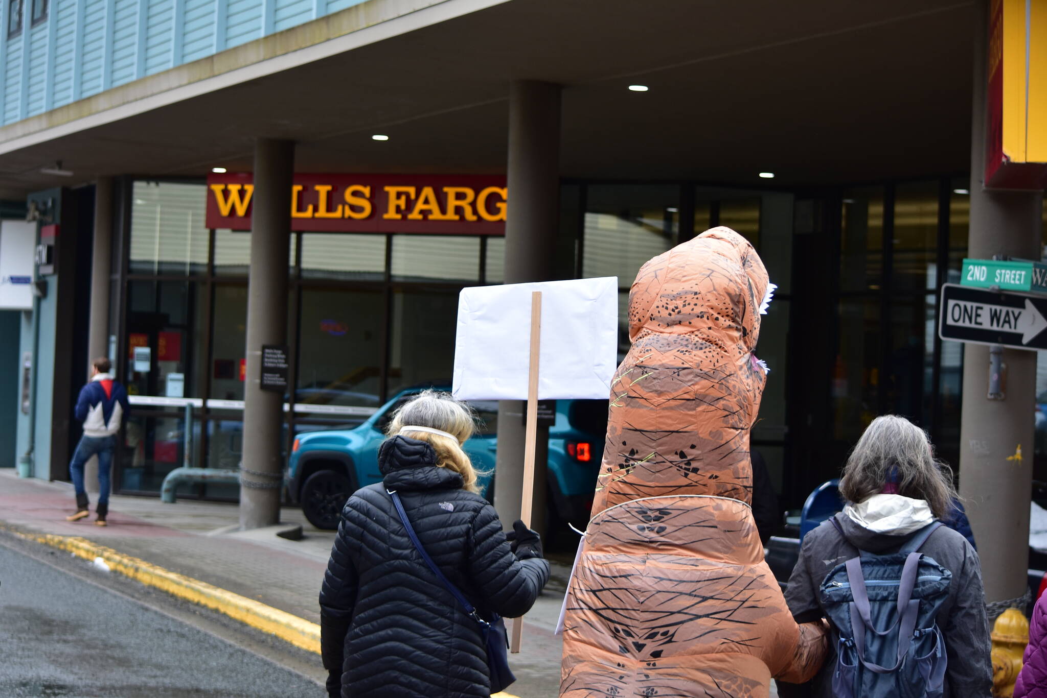 Environmental activists from 350Juneau, one dressed in a dinosaur costume, delivered a letter addressed to the CEO of Wells Fargo to the banks branch in downtown Juneau on Friday, April 2, 2021. The letter called on the bank to divest from fossil fuels. (Peter Segall / Juneau Empire File)