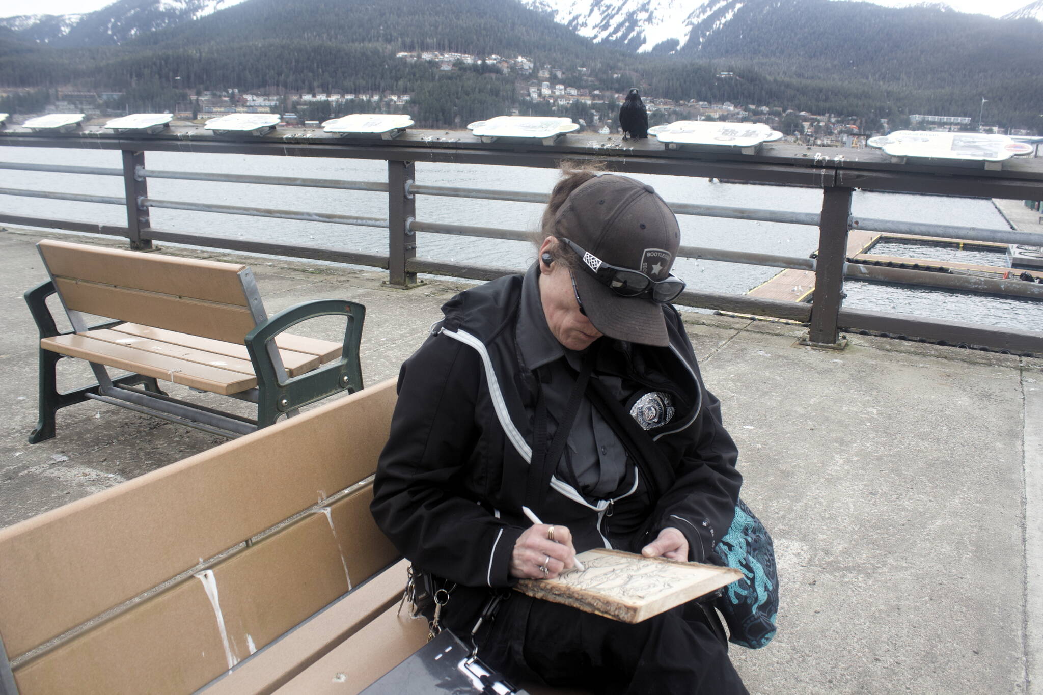 Amy Pervis, a private security officer who’s been a Juneau resident since 2000, sketches a heart and rose for a piece of woodburning art she hopes to sell to tourists this summer on the still mostly empty pier at Marine Park on Friday. (Mark Sabbatini / Juneau Empire)