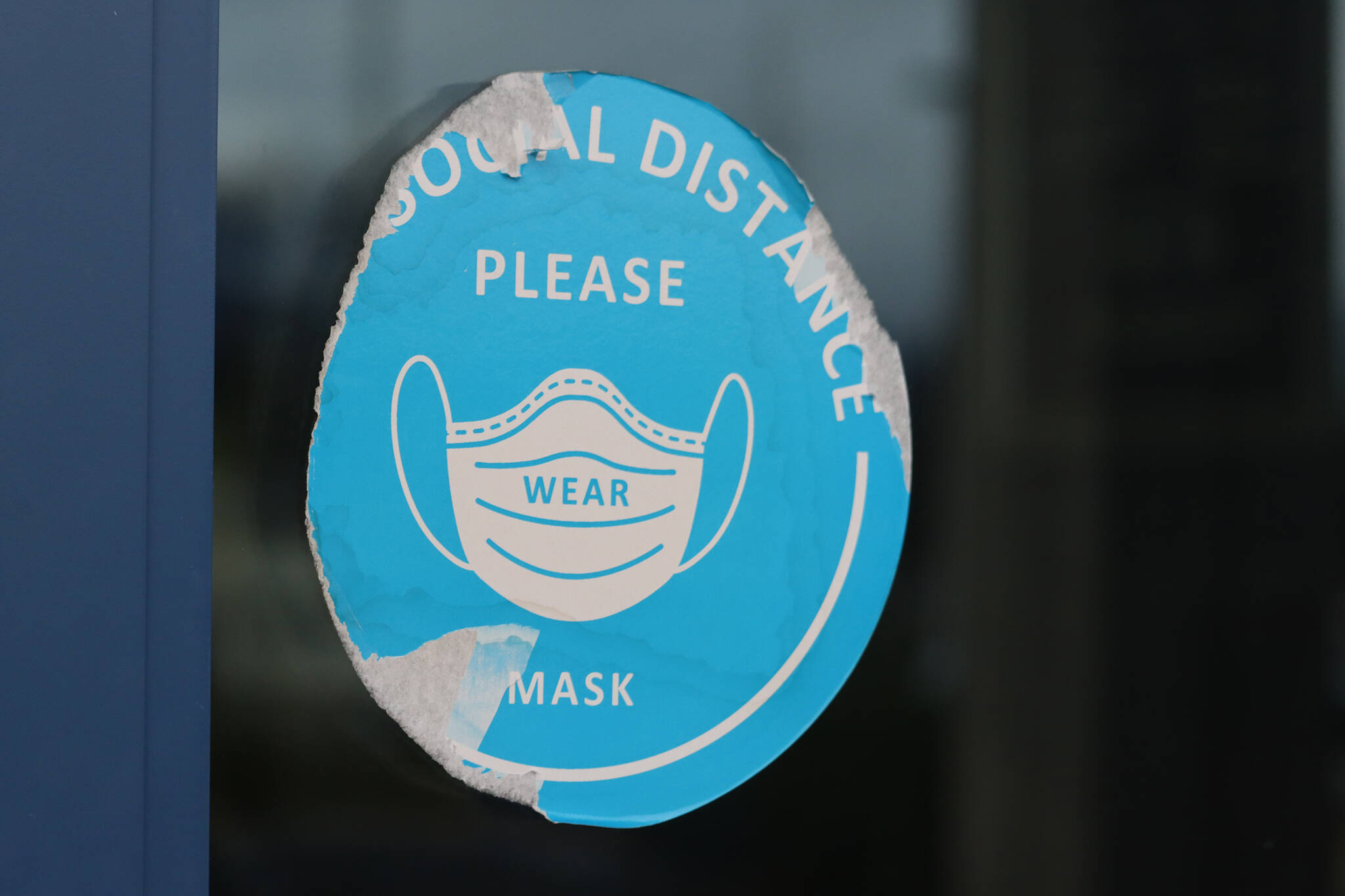 A damaged sticker on a door at Thunder Mountain High School reminds people to social distance and wear masks inside the building. The Juneau School District Board of Education on Tuesday voted to make wearing masks optional in schools. (Ben Hohenstatt / Juneau Empire)