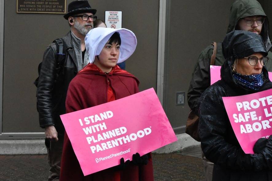 Lisa Denny wears “Handmaid’s Tale”-inspired garb while holding a sign stating “I stand with Planned Parenthood” during a protest held near the Alaska State Capitol on Tuesday, May 3, following a leaked draft of a Supreme Court decision that would overturn the landmark case Roe v. Wade. (Peter Segall / Juneau Empire)