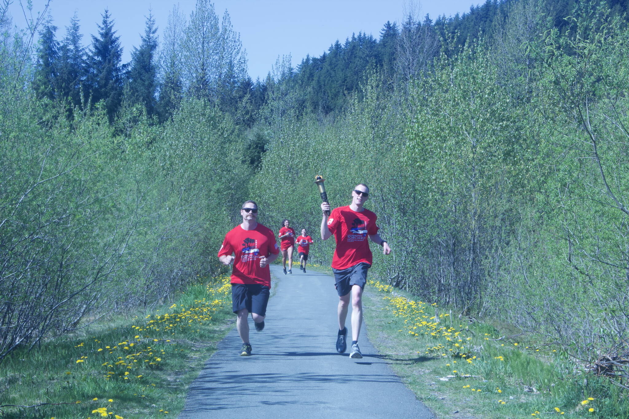Branden Forst, right, carries the torch alongside other law enforcement officers on the trail portion of the Alaska Law Enforcement Torch Run in Juneau on Saturday. (Mark Sabbatini / Juneau Empire)