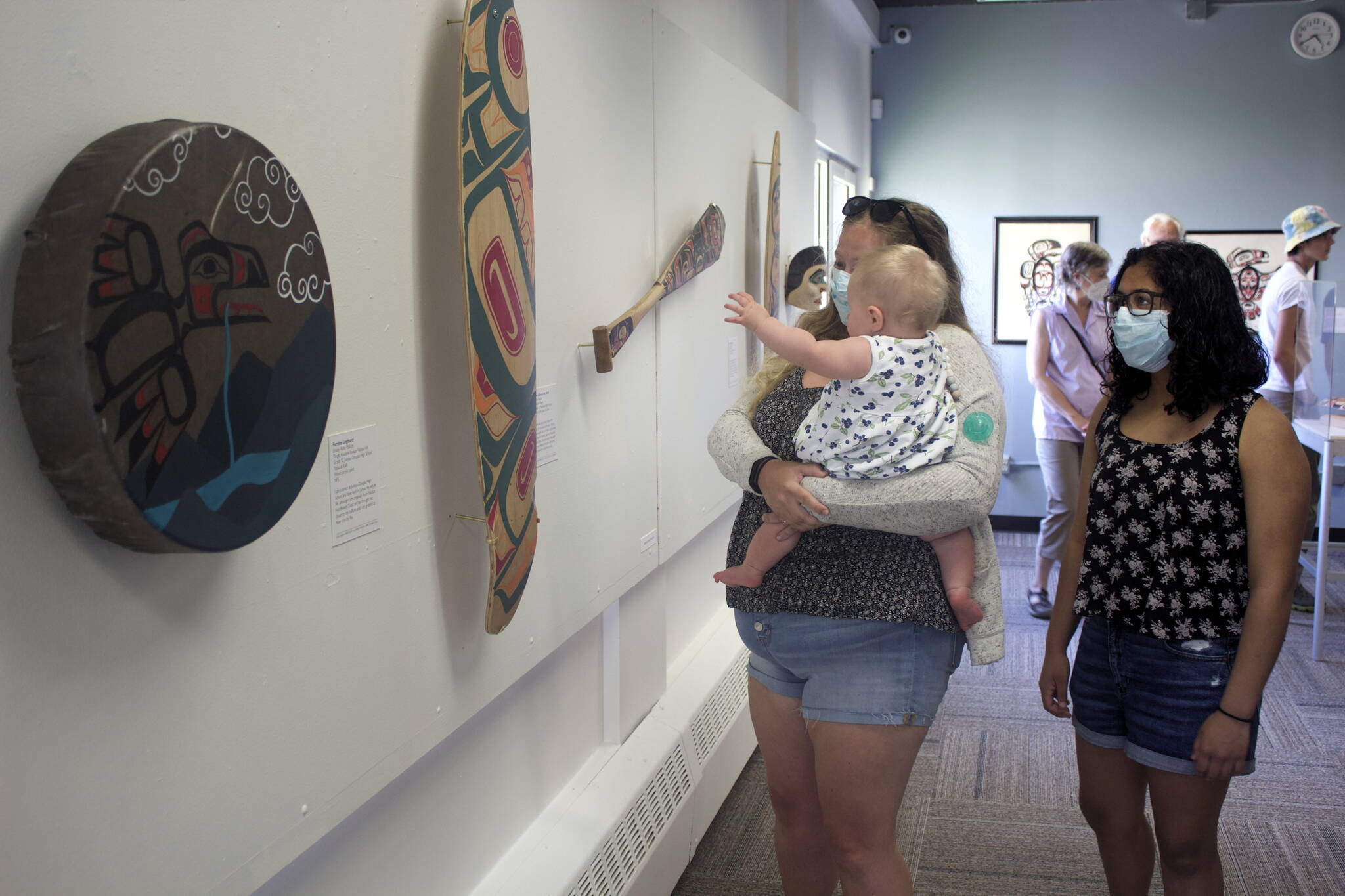 Kristall Bullock, 16, right, a Ketchikan resident whose Native-themed vest is part of the Sealaska Heritage Juried Youth Art Exhibit, examines works by her peers during the debt of the exhibit Friday at the Juneau Arts and Humanities Council. She said she saw works at the exhibit during Celebration in 2018, when she was with one of the dance groups, and “I was thinking I want to have a piece.” Viewing other works at the exhibit with Bullock are her sister, Anna Lindgren, and 8-month-old niece, Evelyn. (Mark Sabbatini / Juneau Empire)