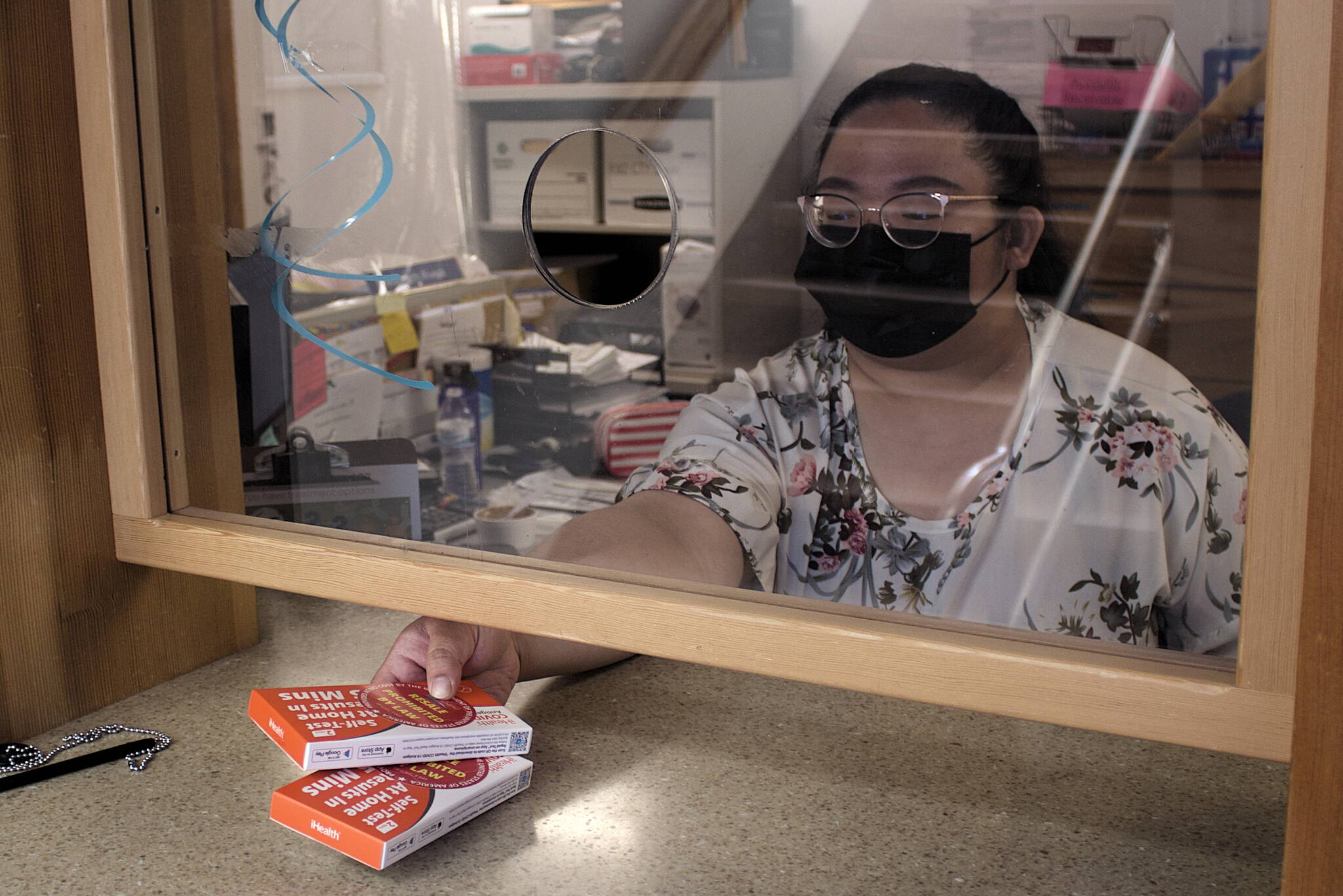 Divina Rotano, a cashier for the city, provides two COVID-19 rapid antigen self test kits at the entrance counter of City Hall on Thursday. The city is also making 24,000 tests arriving from the federal government this week available at public libraries, the Juneau Police Department and Juneau Public Health Center. (Mark Sabbatini / Juneau Empire)
