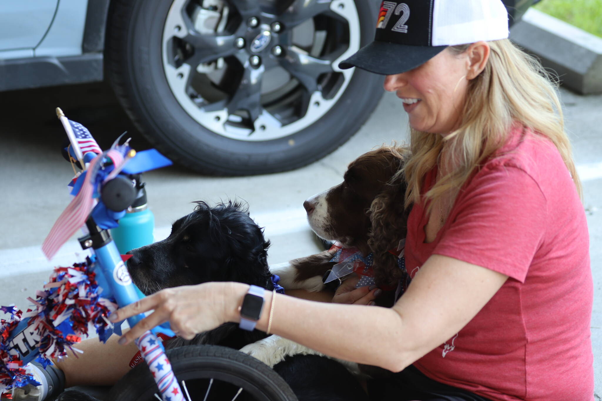 Holly Johnson, with help from dogs Hazel and Stella, decorates a bike during the Douglas Fourth of July Committee’s annual Bicycle Decorating session held at the Douglas Public Library on July 2, 2022. (Michael S. Lockett / Juneau Empire)