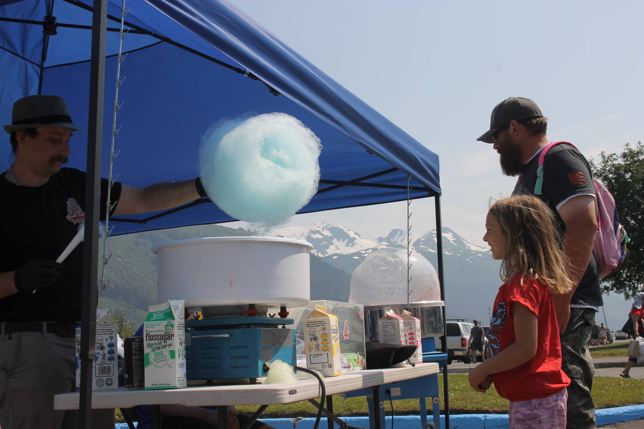 Mia Halloway, 6, grabs a cotton candy with her dad in Savikko Park. A long string of kids stood in line to grab a cotton candy from the Twhrly Whrliy Cotton Candy stand on a bright and sunny Fourth of July afternoon. (Clarise Larson / Juneau Empire)