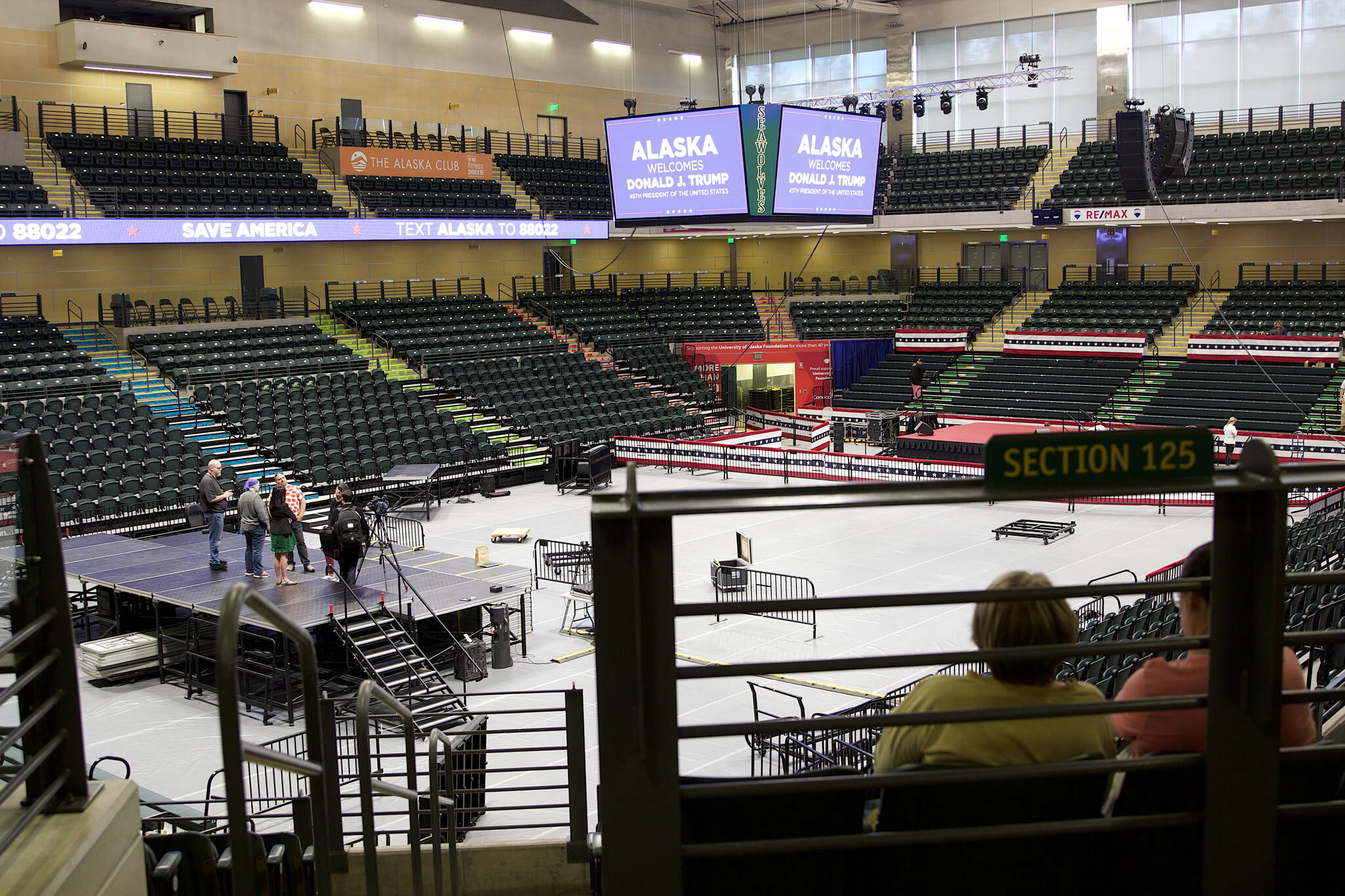 A couple of visitors watch preparations Friday afternoon for the Save America Rally scheduled Saturday at the Alaska Airlines Center in Anchorage. (Mark Sabbatini / Juneau Empire)
