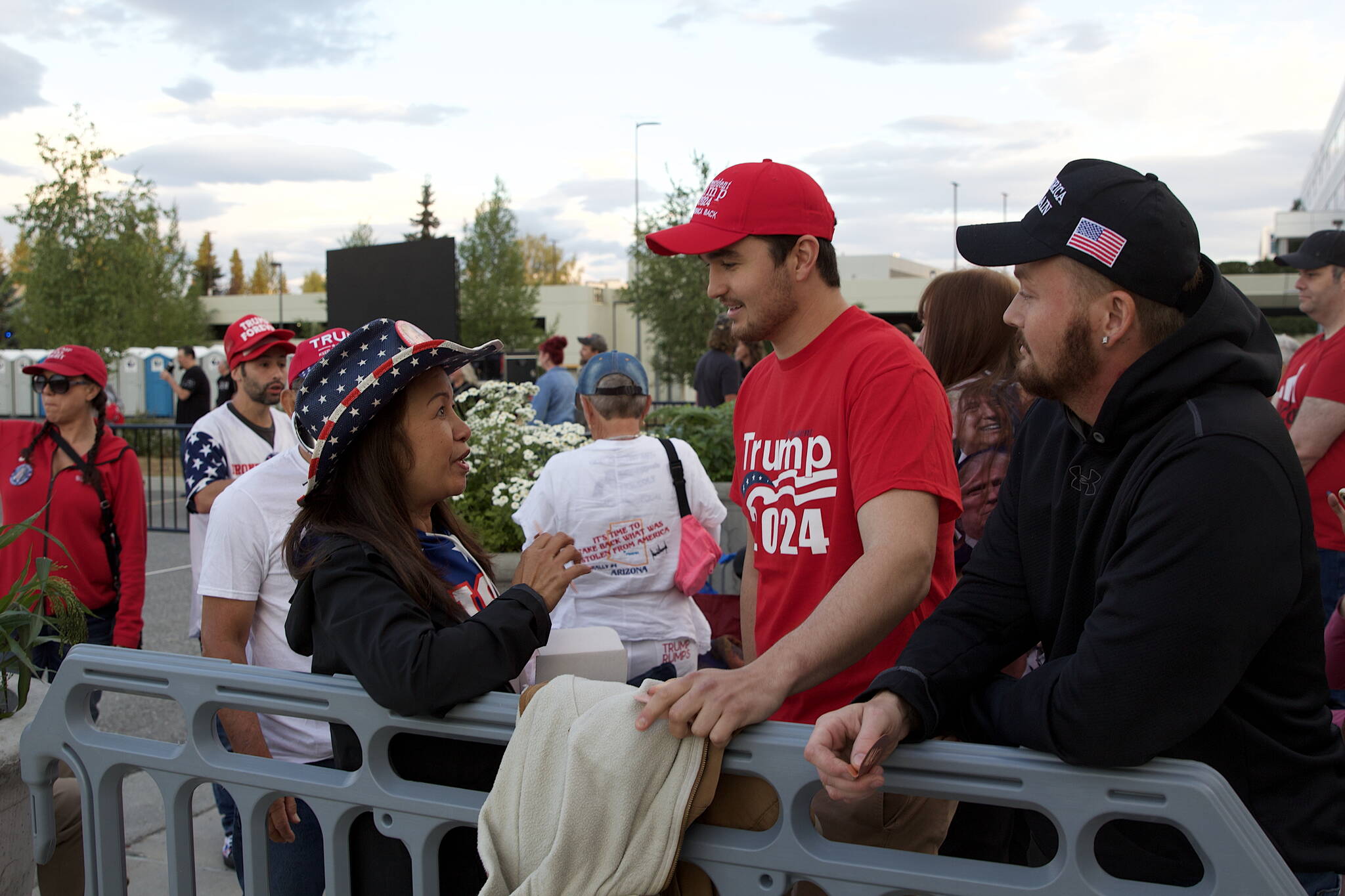 Amy Lee, left, a Vietnam native now living in San Diego, offers one of her custom sold-copper "MAGA" fish to Anchorage residents Kenny Gentry and Hunter Kern at about 5:30 a.m. Saturday outside the Alaska Airlines Center. They were among the first in line for the Save America Rally that started more than seven hours later.
(Mark Sabbatini / Juneau Empire)