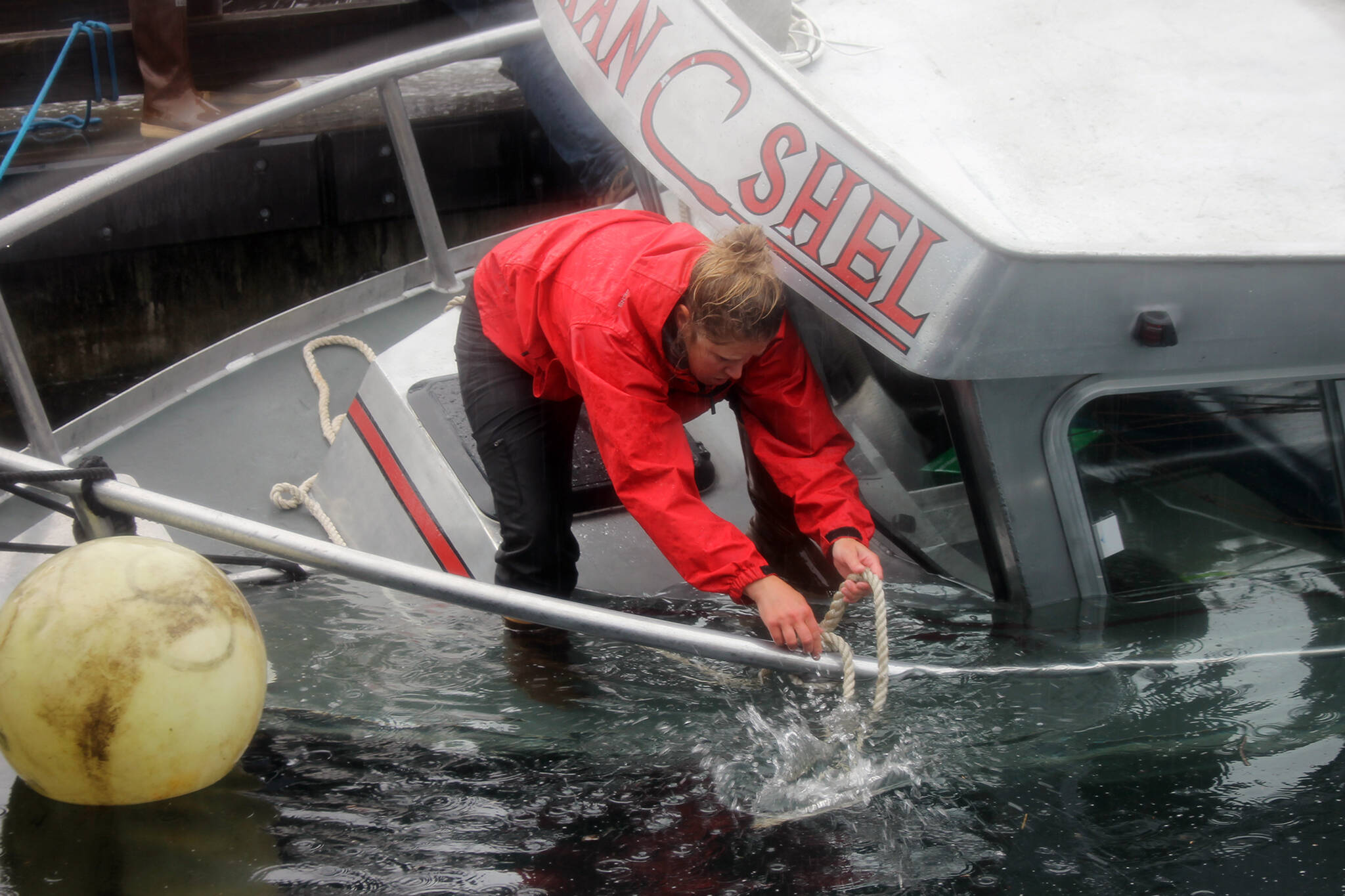 Shelby Martin the, co-owner of the Alaskan Shel, stands at the bow of her boat as it sinks while docked at the Don D. Statter Harbor. (Clarise Larson / Juneau Empire)