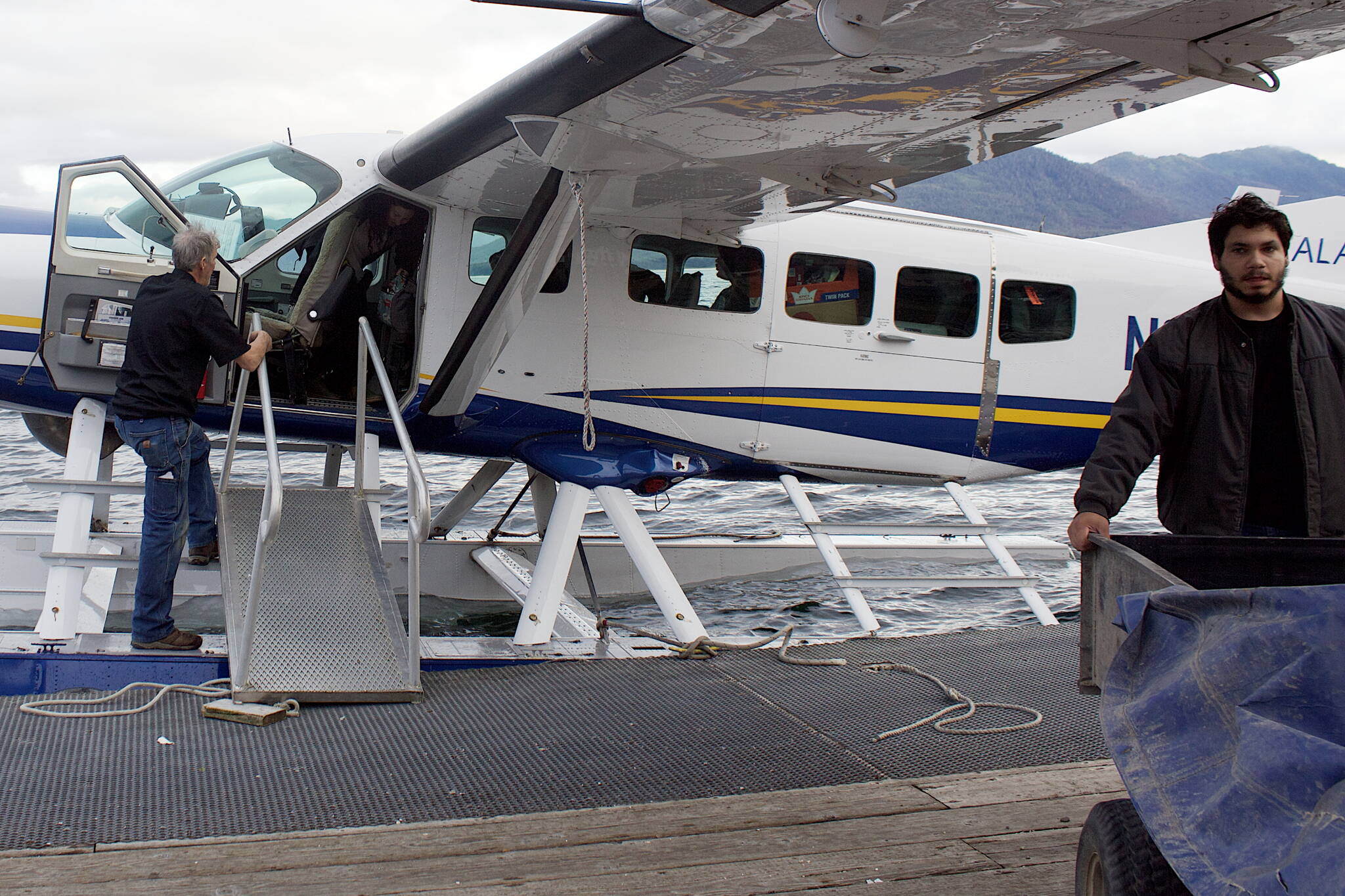 Jerusalem Chase, 22, right, manager at the Alaska Seaplanes terminal in Tenakee Springs, hauls cargo from an arriving flight Sunday night to the ATV he uses to deliver items to passengers. Traditional road vehicles are banned in Tenakee except for a couple of public service trucks, but ATVs are increasingly in use.