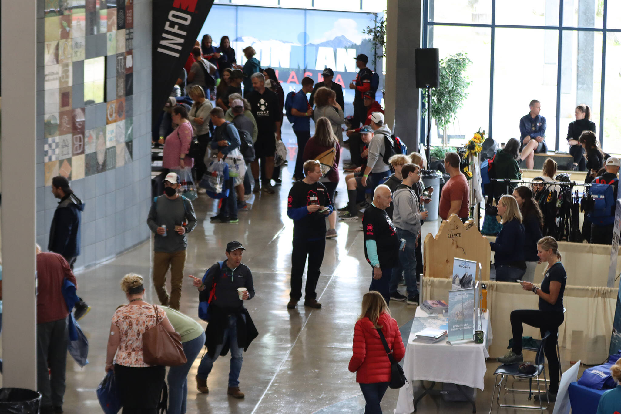 Athletes and race supporters walk the foyer of Thunder Mountain High School to visit the various Ironman and local booths open at the Ironman Village. (Ben Hohenstatt / Juneau Empire)