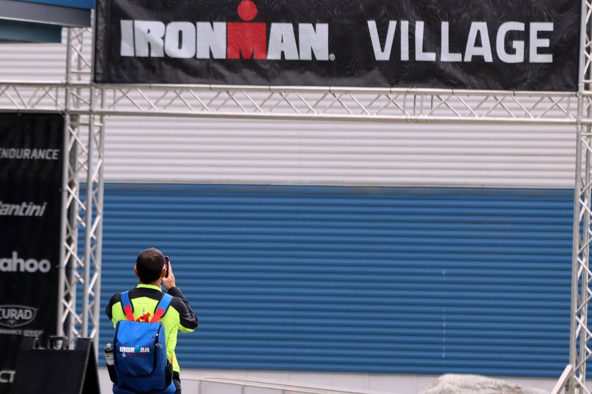 An athlete takes a photo of the Ironman Village sign placed at the entrance of Thunder Mountain High School on Thursday afternoon. (Ben Hohenstatt / Juneau Empire)