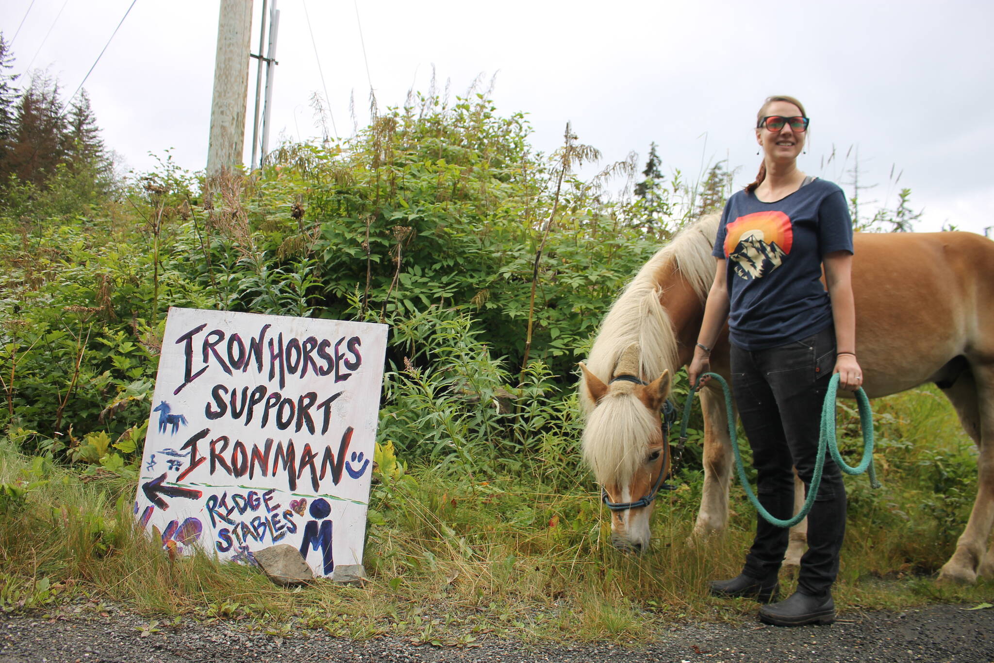 Keegan Carroll, a wellness coach for Jamhi Health and Wellness, stands with Mr. Higgins, a large pony at Ridge Stables LLC owned by Chava Lee, a long Glacier Highway to show support for the bikers. (Clarise Larson/ Juneau Empire)