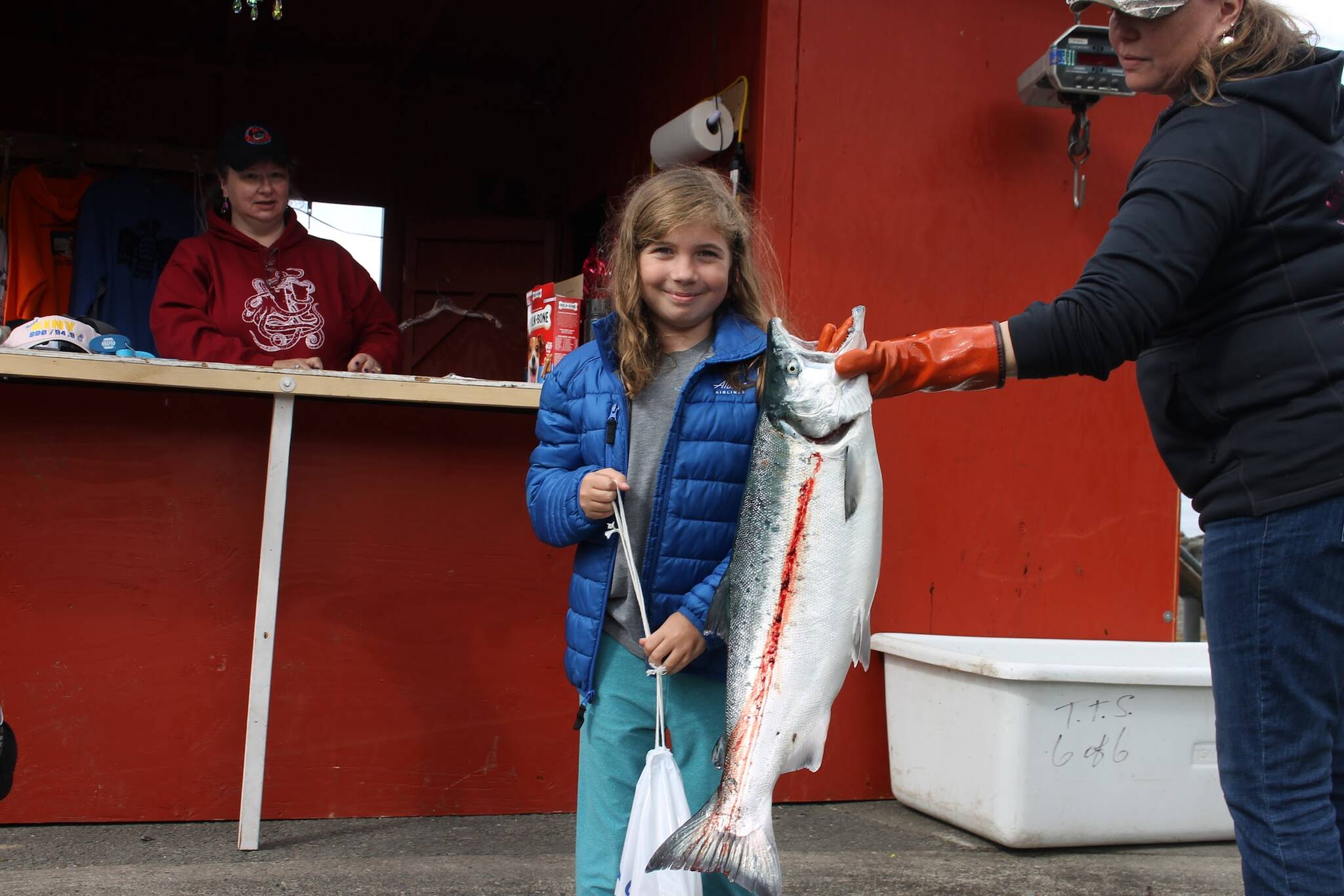 Grace Frederick stands in front of the Amalga Harbor weigh in station next to her 11.8-pound coho salmon she caught with the help of her father, Brian. (Clarise Larson / Juneau Empire)