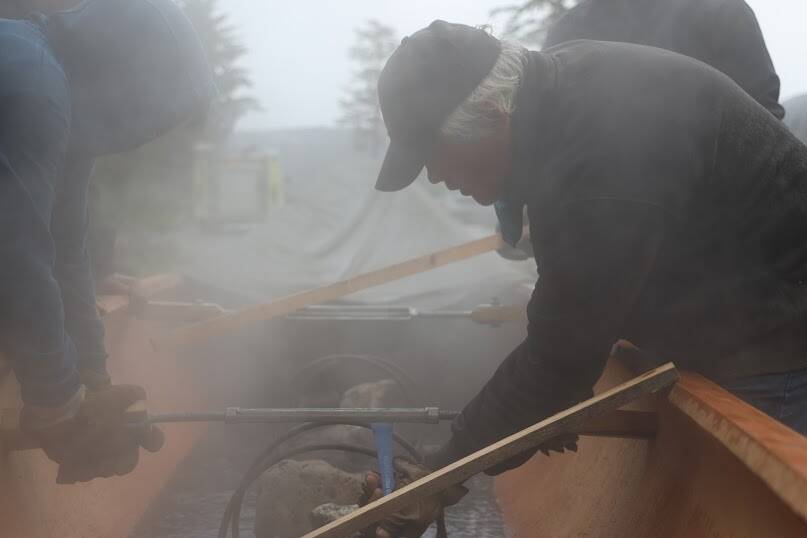 Wayne Price leans through the smoke to turn the an expanding device running across the width of the dugout canoe. The canoe only suffered from one crack during the expanding process, which Price said is common and can be easily fixed. (Clarise Larson / Juneau Empire)