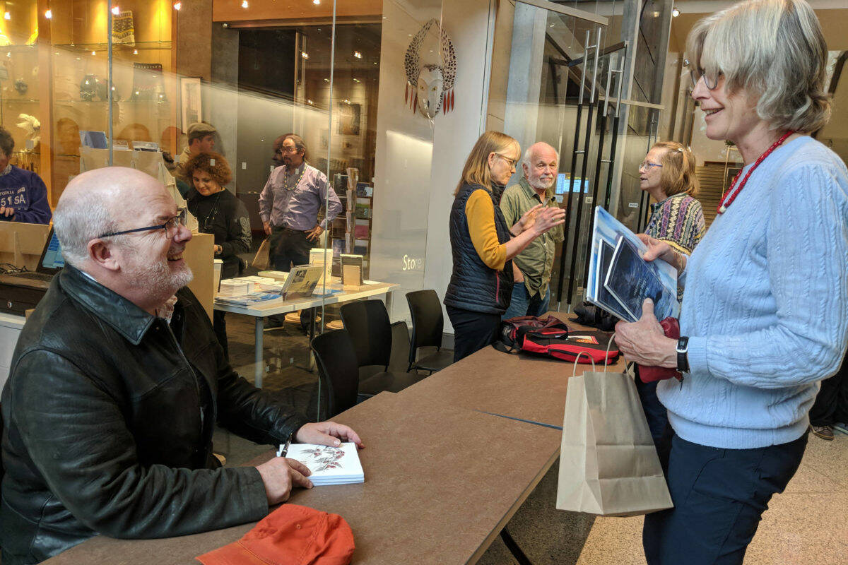 In this October 2018 photo, author John Straley prepares to sign a book for author Heather Lende after the Alaska Literary Festival at the Father Andrew P. Kashevaroff Building in Juneau. They were both speakers at the event. Straley is a former Alaska State Writer Laureate, while Lende is the current State Writer Laureate. (Ben Hohenstatt / Juneau Empire File)