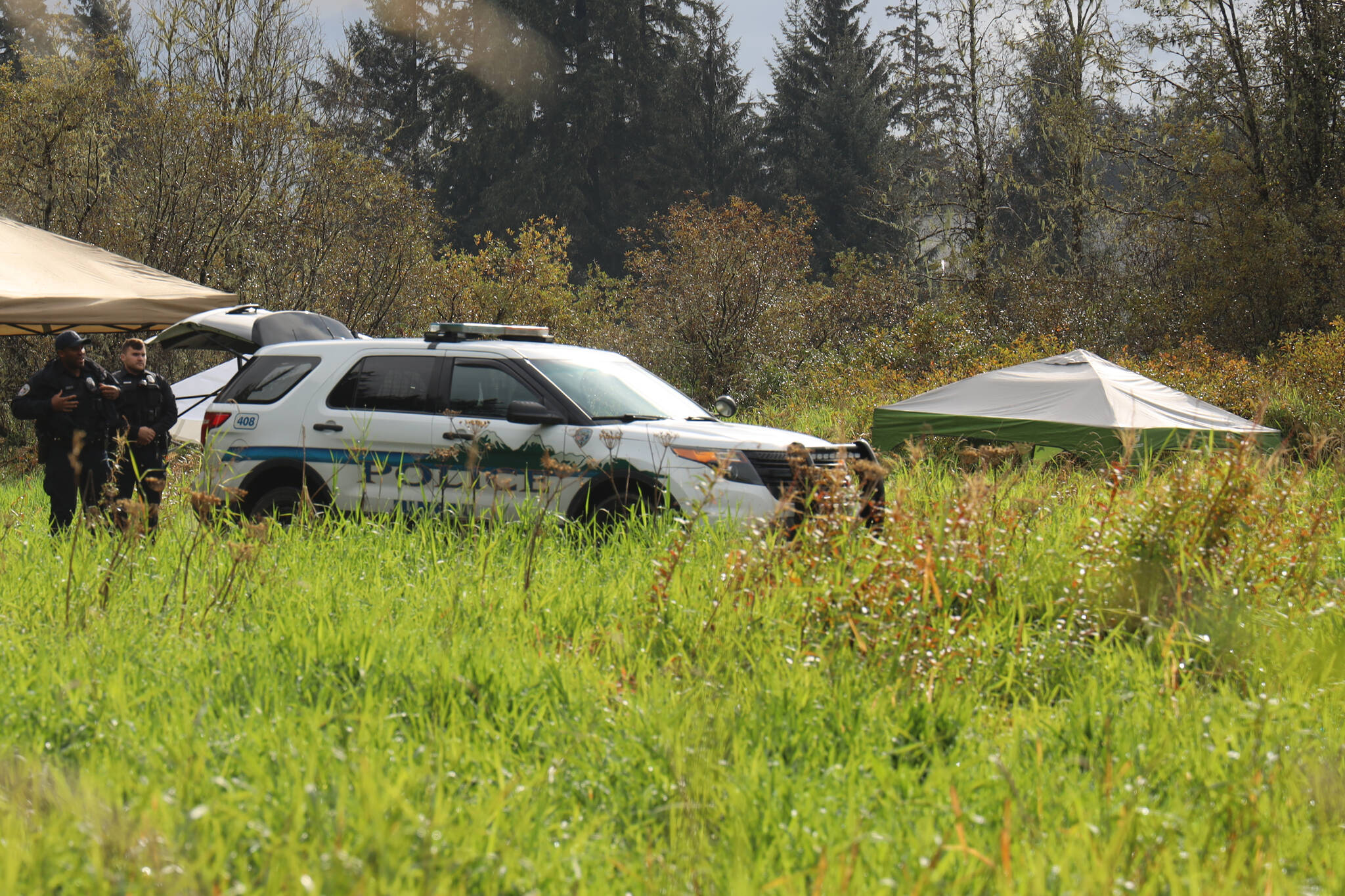 On Thursday morning, JPD Officer Austin Thomas and Officer Taylor Davis walk the fielded area which was blocked off by crime scene tape. Multiple tents and a police vehicle sat in the field where the tape surrounded, another police vehicle sat in a dirt parking area. (Clarise Larson / Juneau Empire)