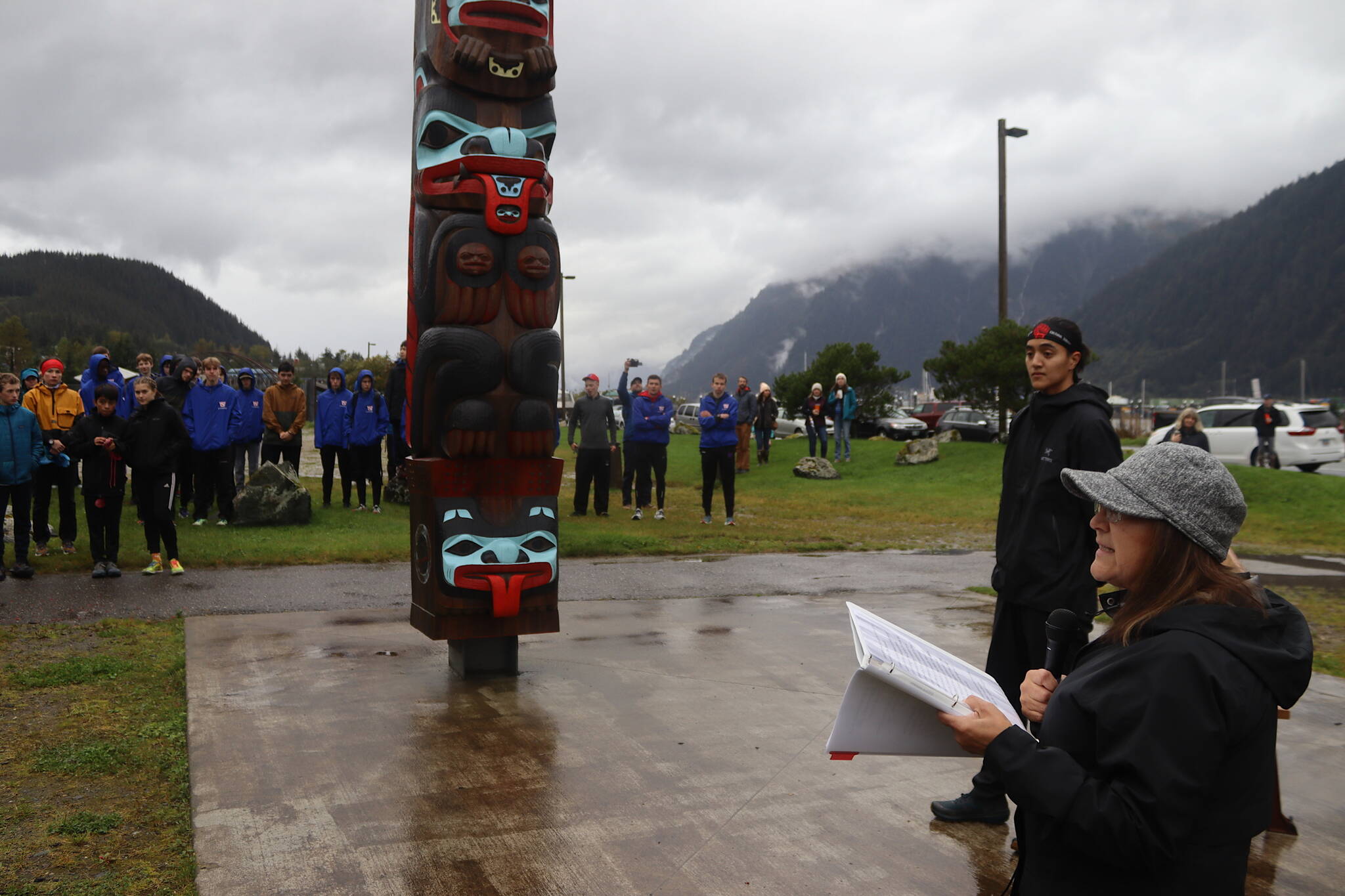 Kitty Eddy, a longtime Tlingit language education leader in Juneau, offers a welcoming message to about 250 cross-country competitors and coaches from Southeast Alaska high schools at the totem pole at A Káx Yaa Andagan Yé (Sandy Beach) before the Capital City Invite on Saturday morning. (Mark Sabbatini / Juneau Empire)