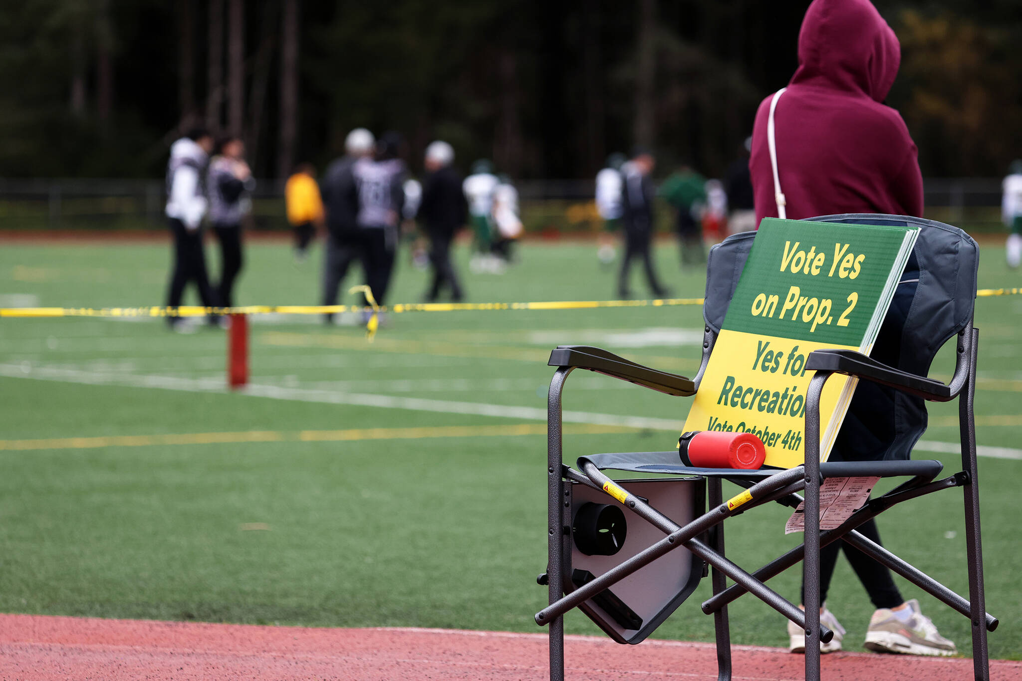 Signs urging Saturday football game attendees to vote in favor of Proposition 2 sit on a chair on the track at Adair-Kennedy Memorial Park. (Ben Hohenstatt / Juneau Empire)