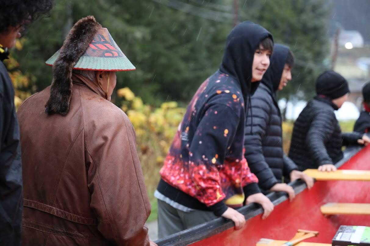 On Wednesday morning, Tlingit master carver Wayne Price stands alongside students as they push the 30-foot-long dugout canoe he spent the last year creating. (Clarise Larson / Juneau Empire)